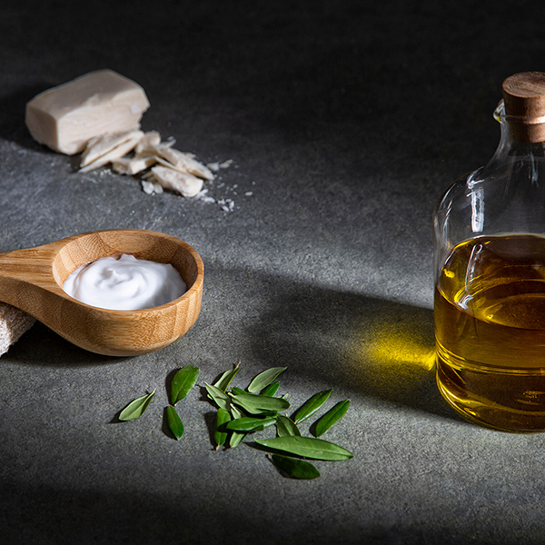 a spoon with a wooden spoon next to a bottle of oil and leaves