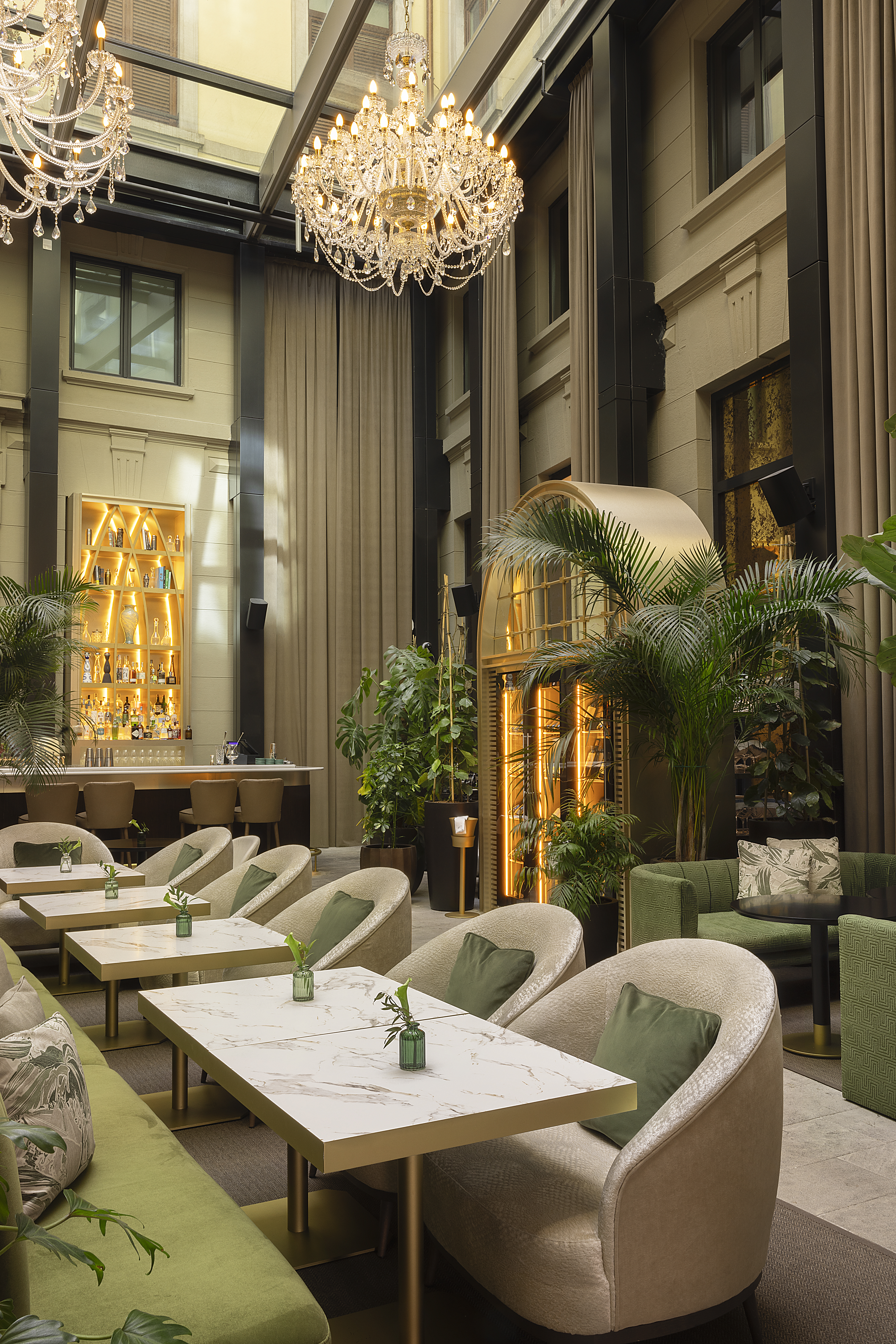 Luxury bar lounge with chandeliers, green seating, marble tables, illuminated bar.