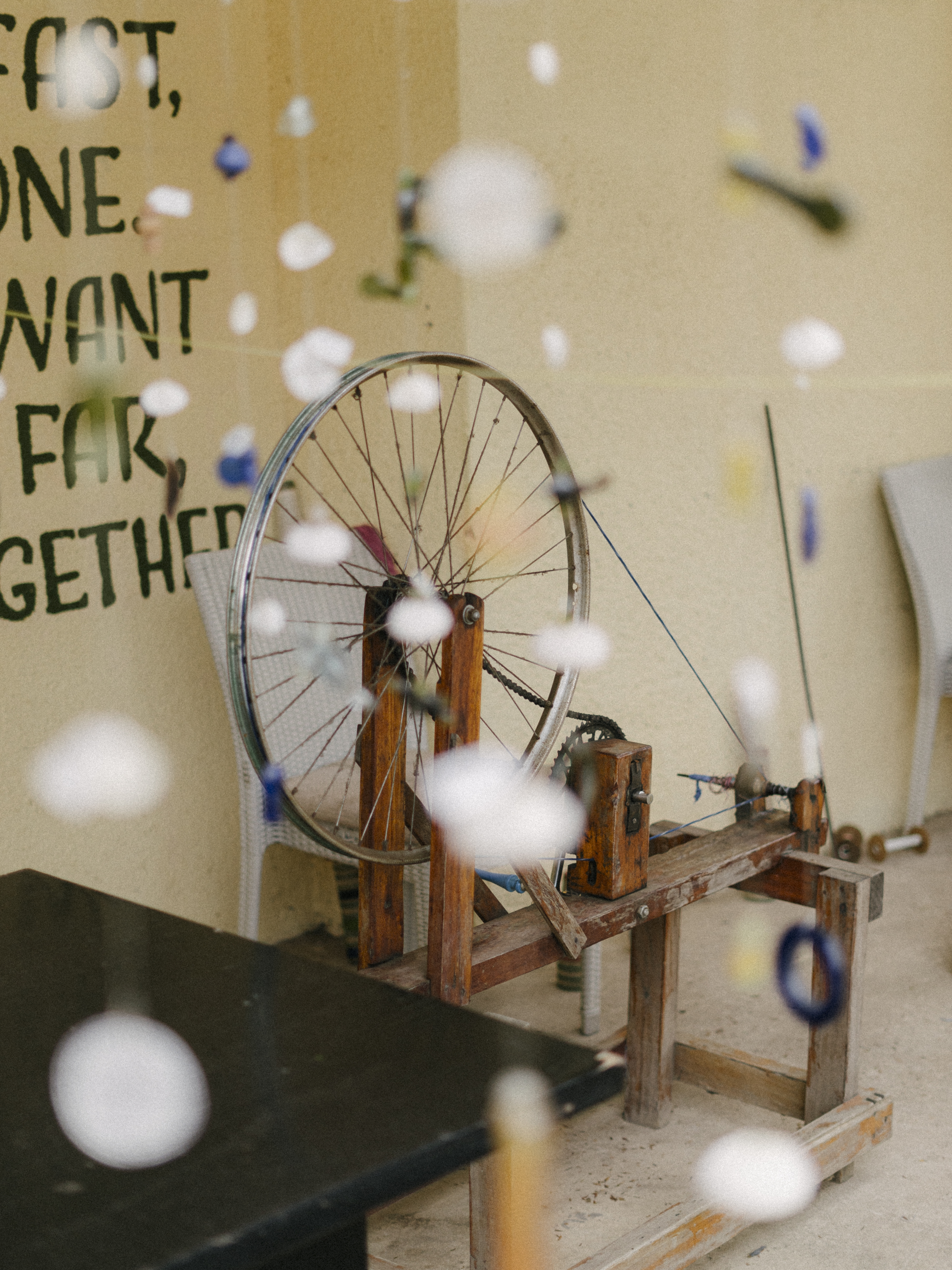 Wooden spinning wheel made with a bicycle wheel, beside a text-covered wall.