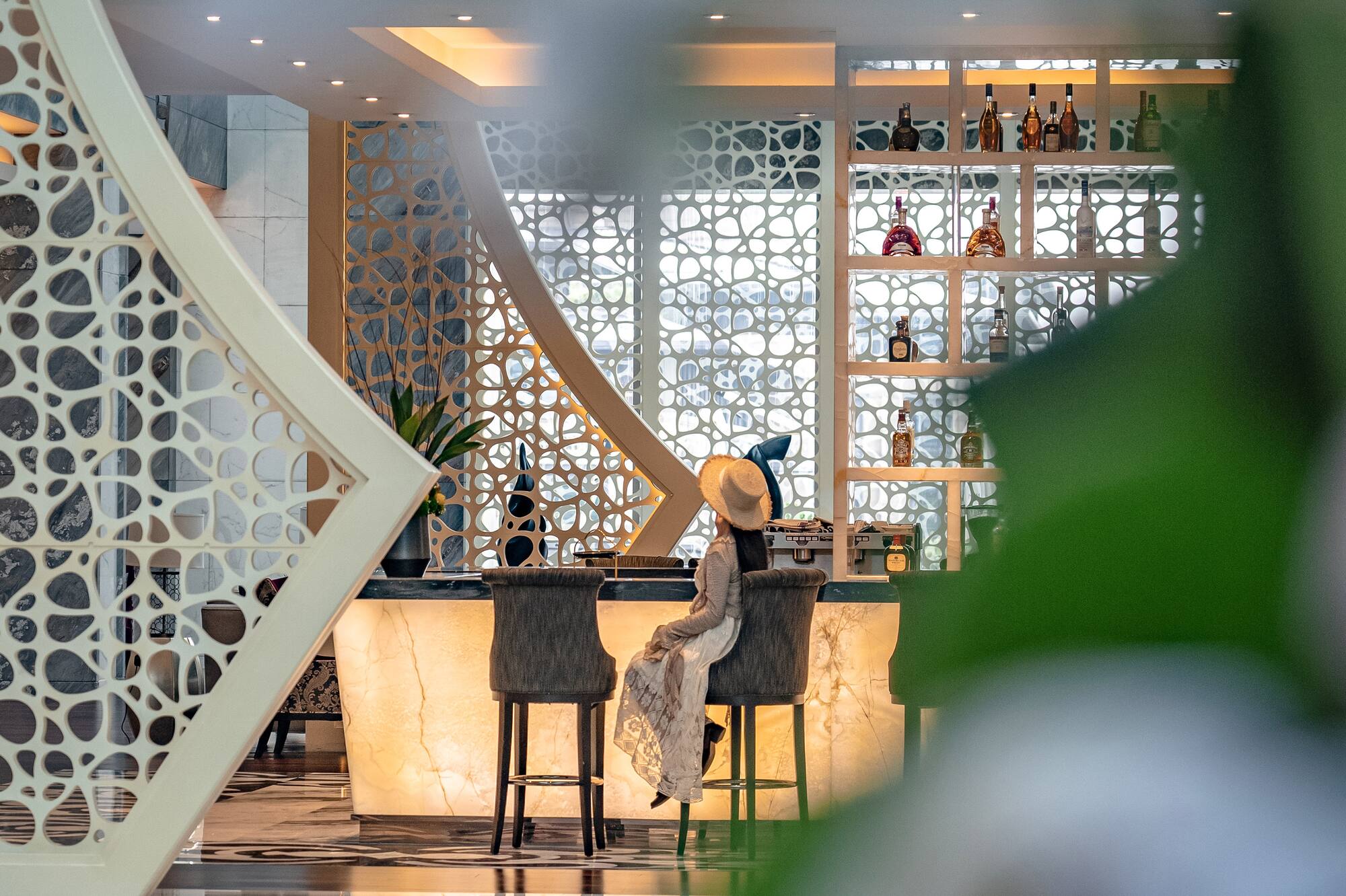 Woman at luxurious backlit bar, modern hotel lounge with ornate screen.