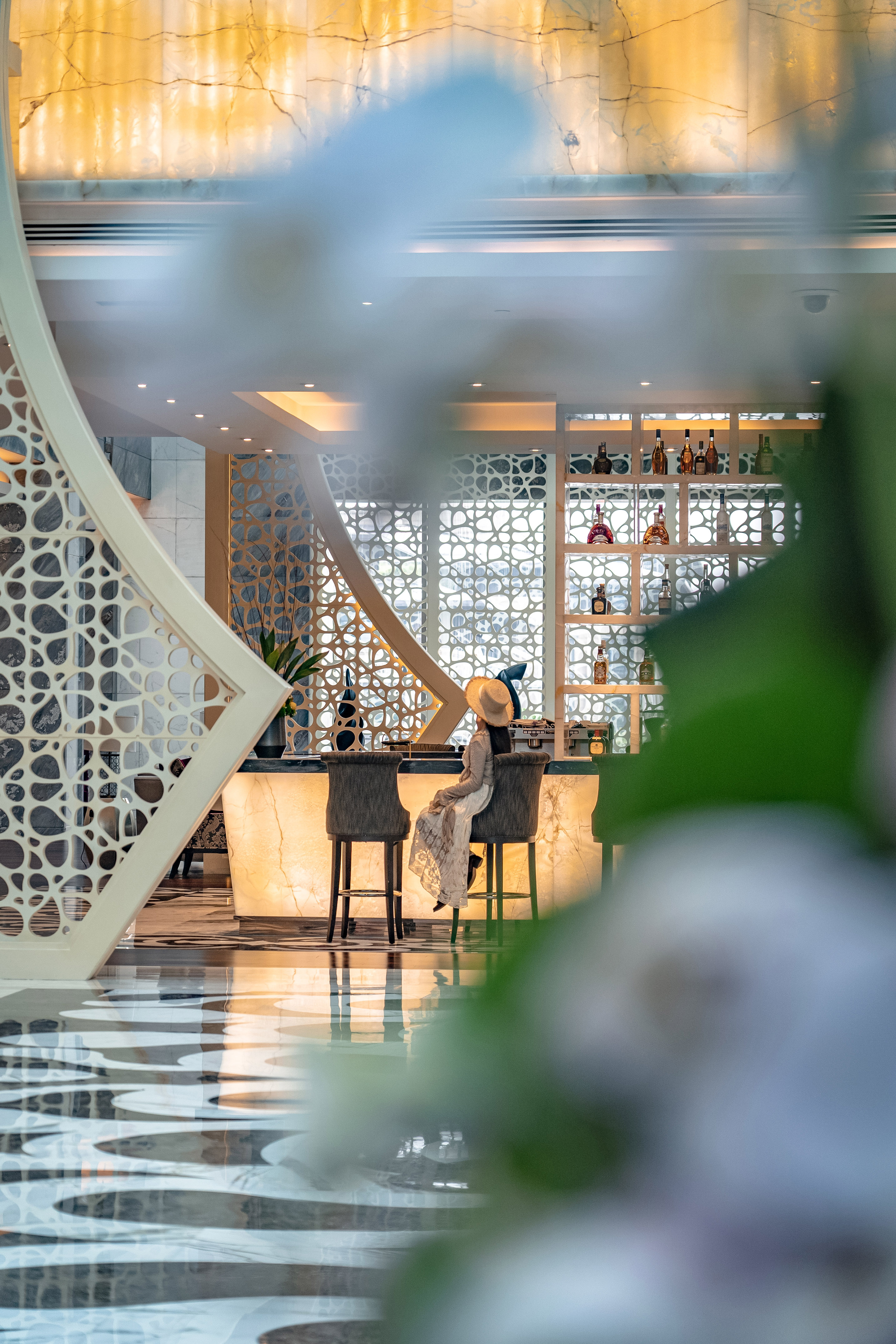 Woman at luxurious backlit bar, modern hotel lounge with ornate screen.