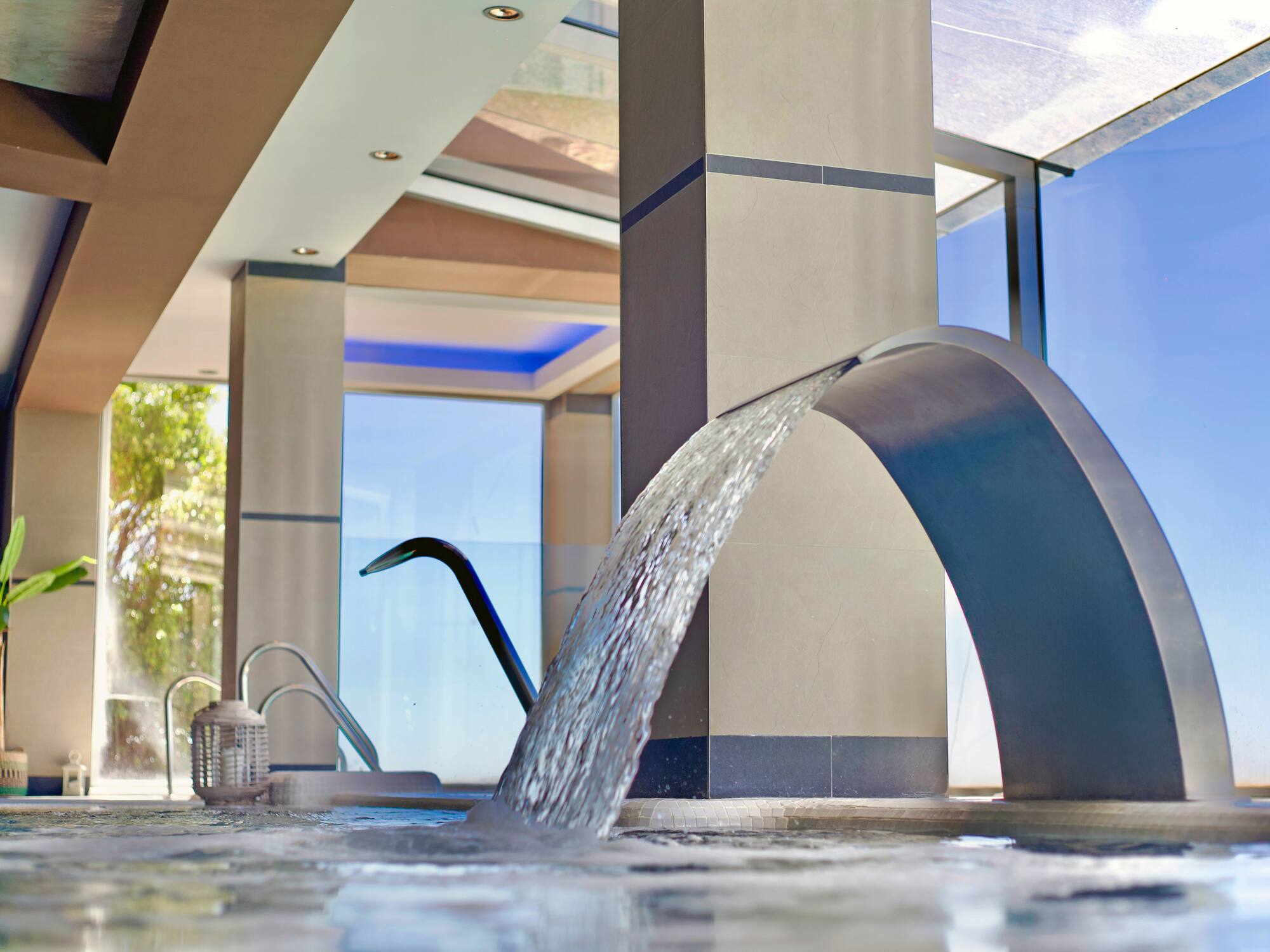 Piscina de spa interior moderna con cascada de agua y luz natural.