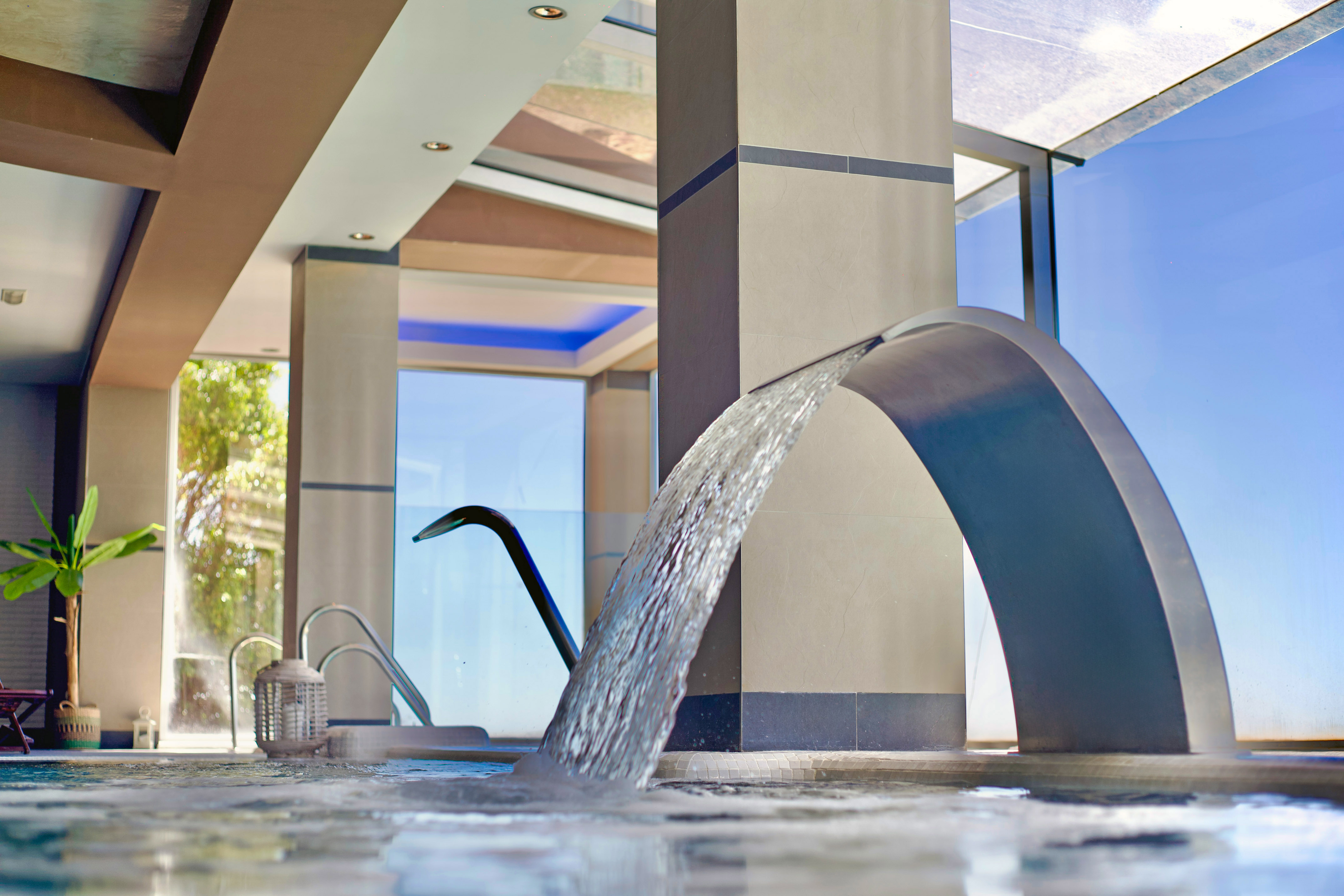 Piscina de spa interior moderna con cascada de agua y luz natural.