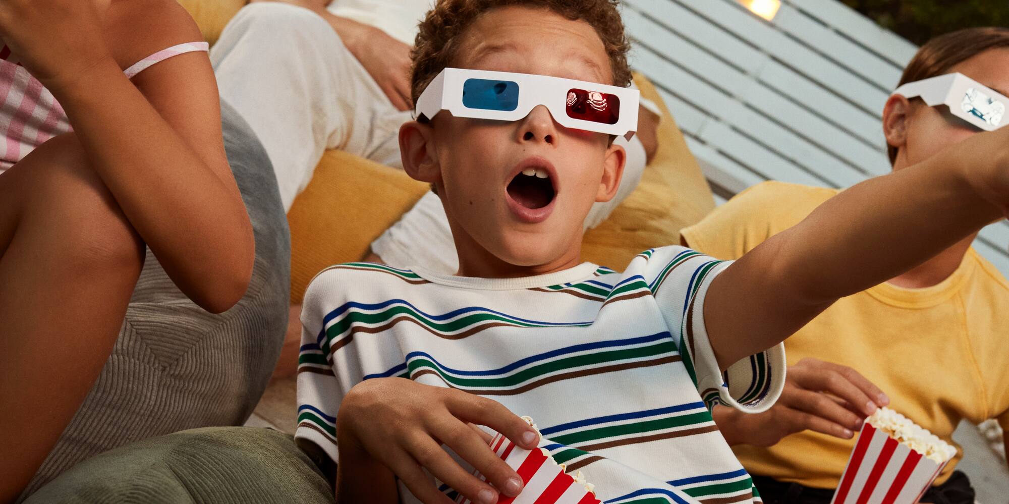 Family enjoying outdoor 3D movie night with popcorn, kids in awe.