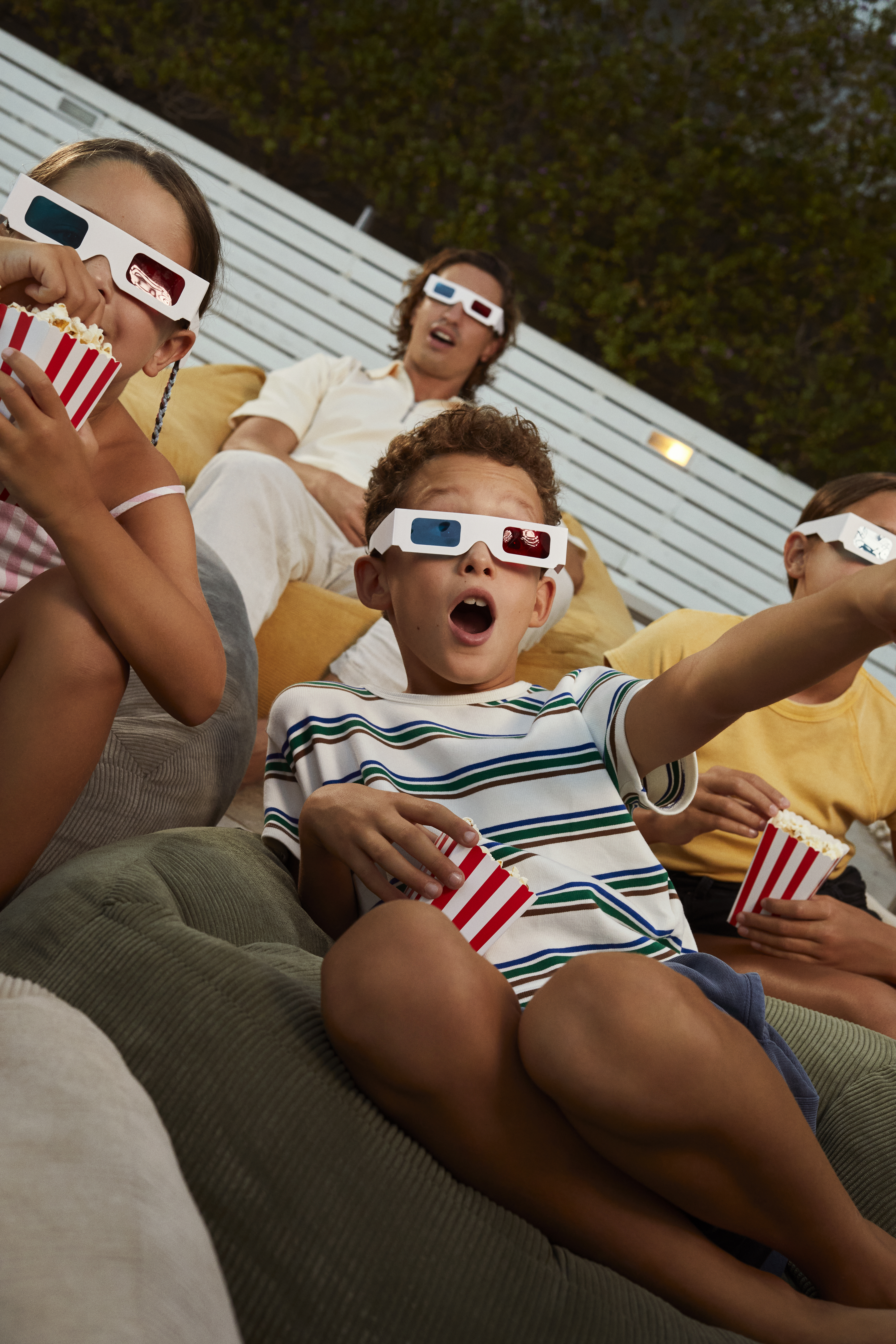 Family enjoying outdoor 3D movie night with popcorn, kids in awe.