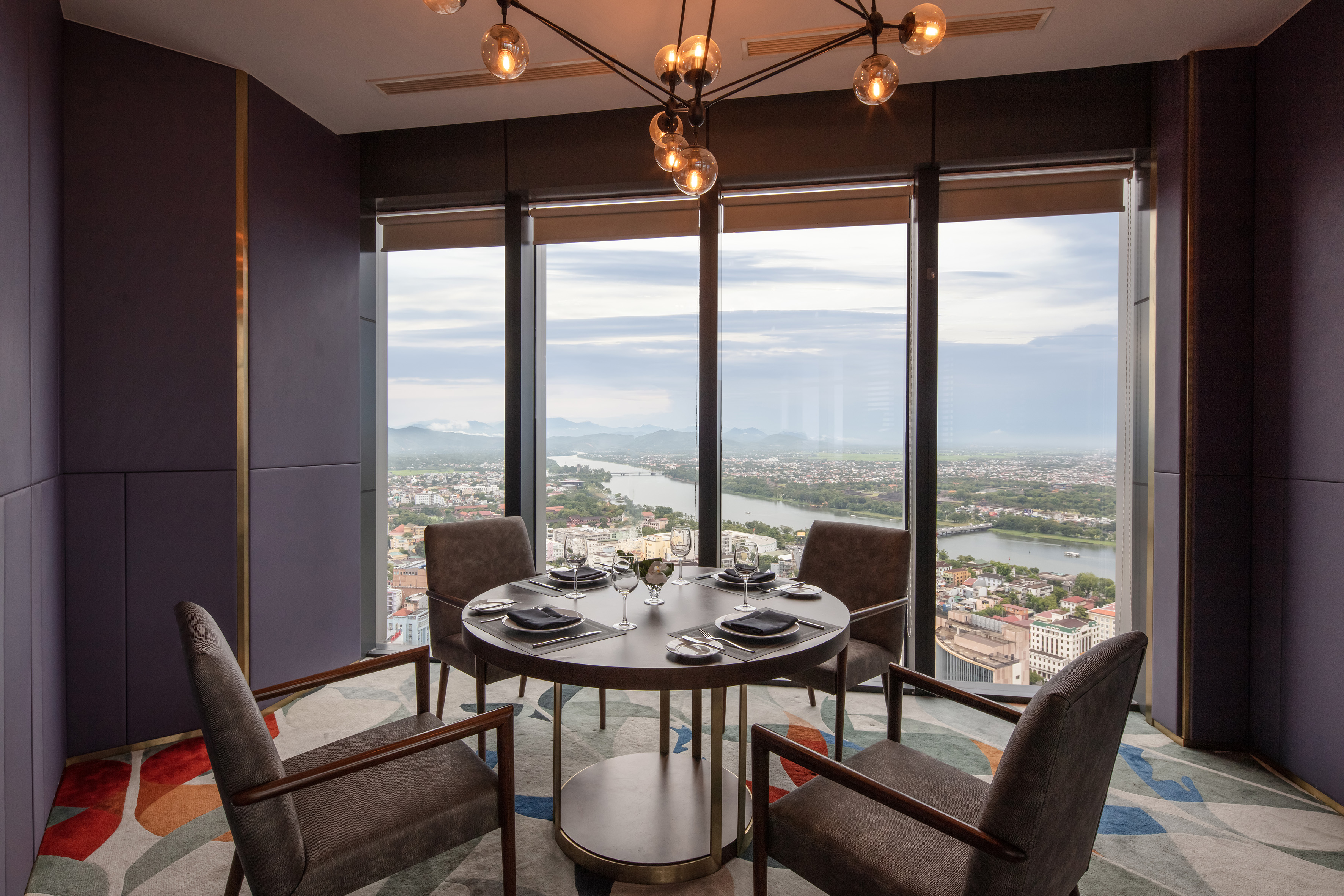 Modern dining room with set table for four, panoramic city and river view.