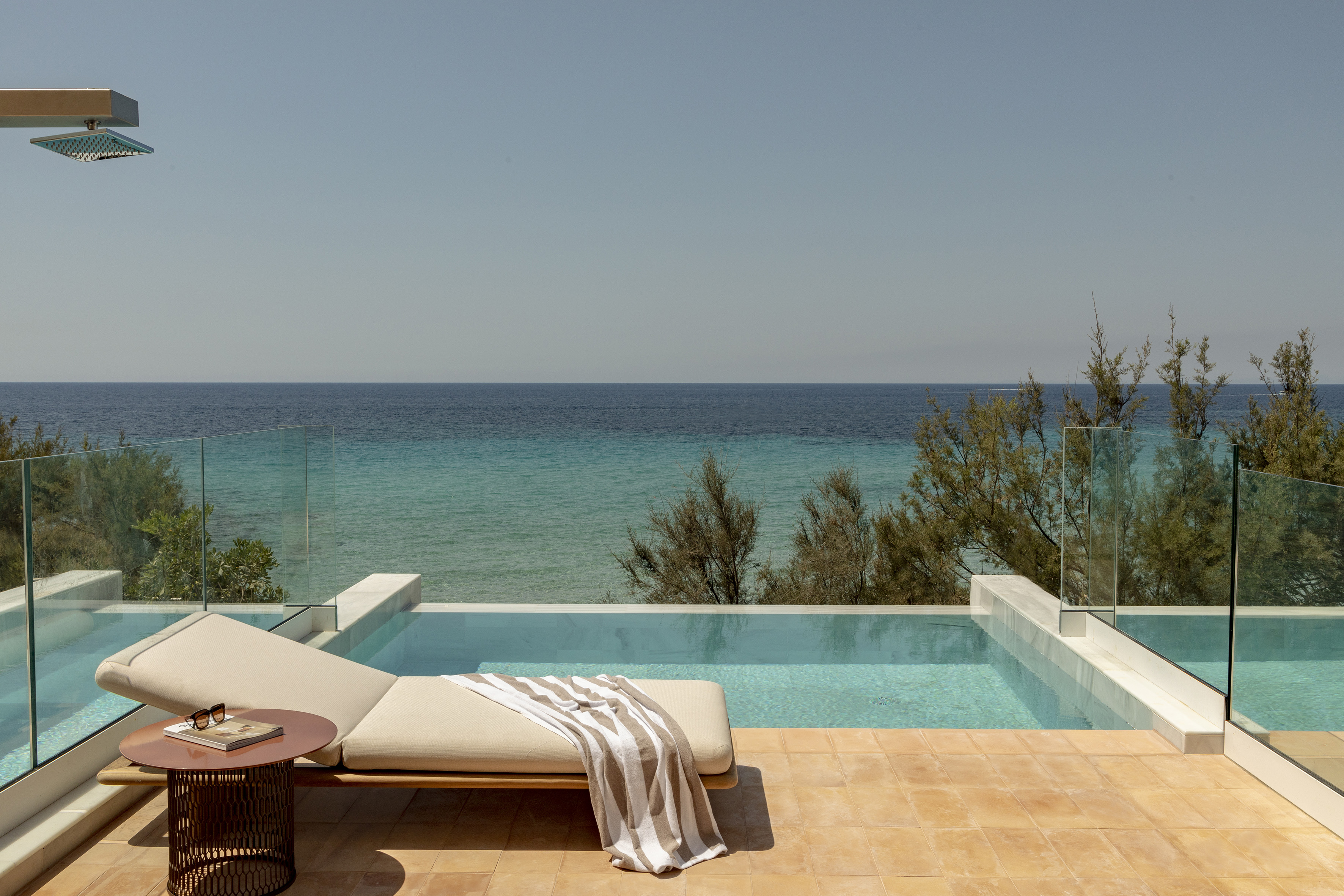 Private infinity pool overlooking the ocean, with sunbed and outdoor shower.
