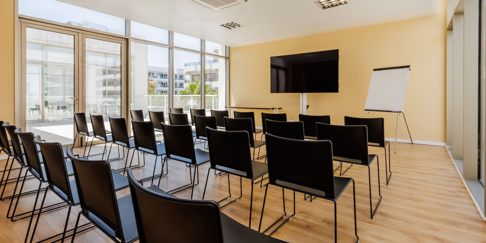 Bright conference room with black chairs, large screen, flip chart, windows.