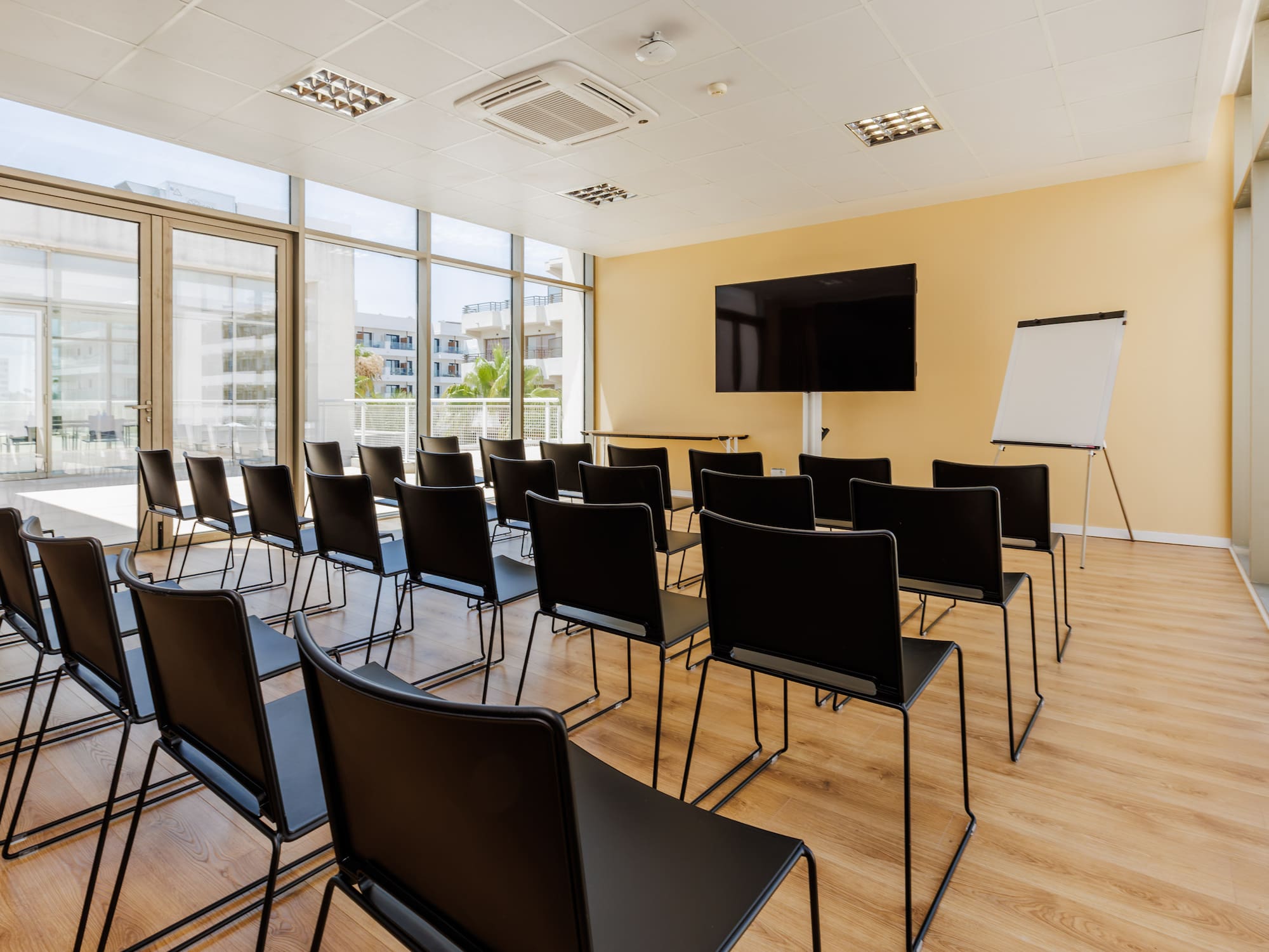 Modern conference room with black chairs, large TV, flip chart, and bright windows.