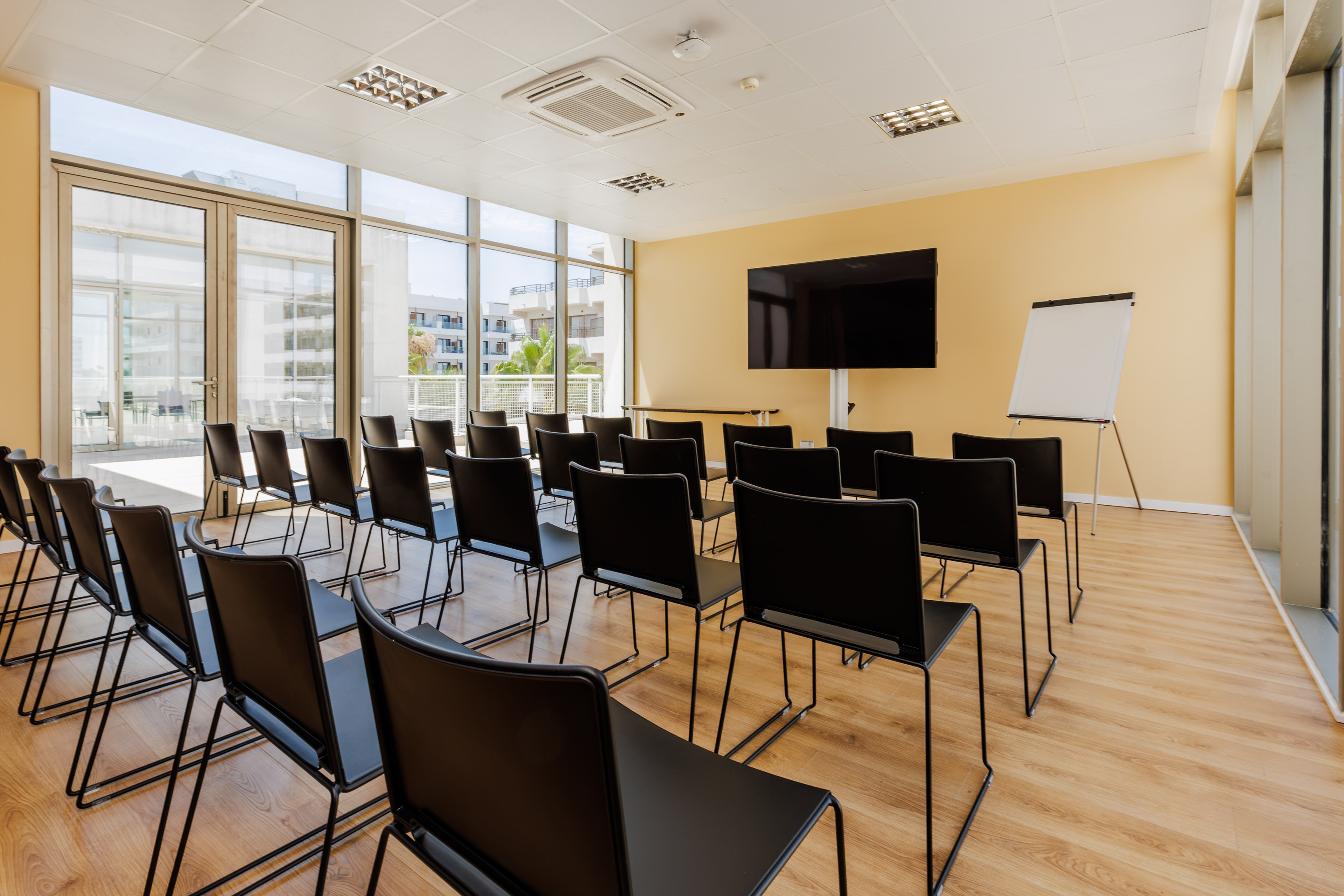 Modern conference room with black chairs, large TV, flip chart, and bright windows.