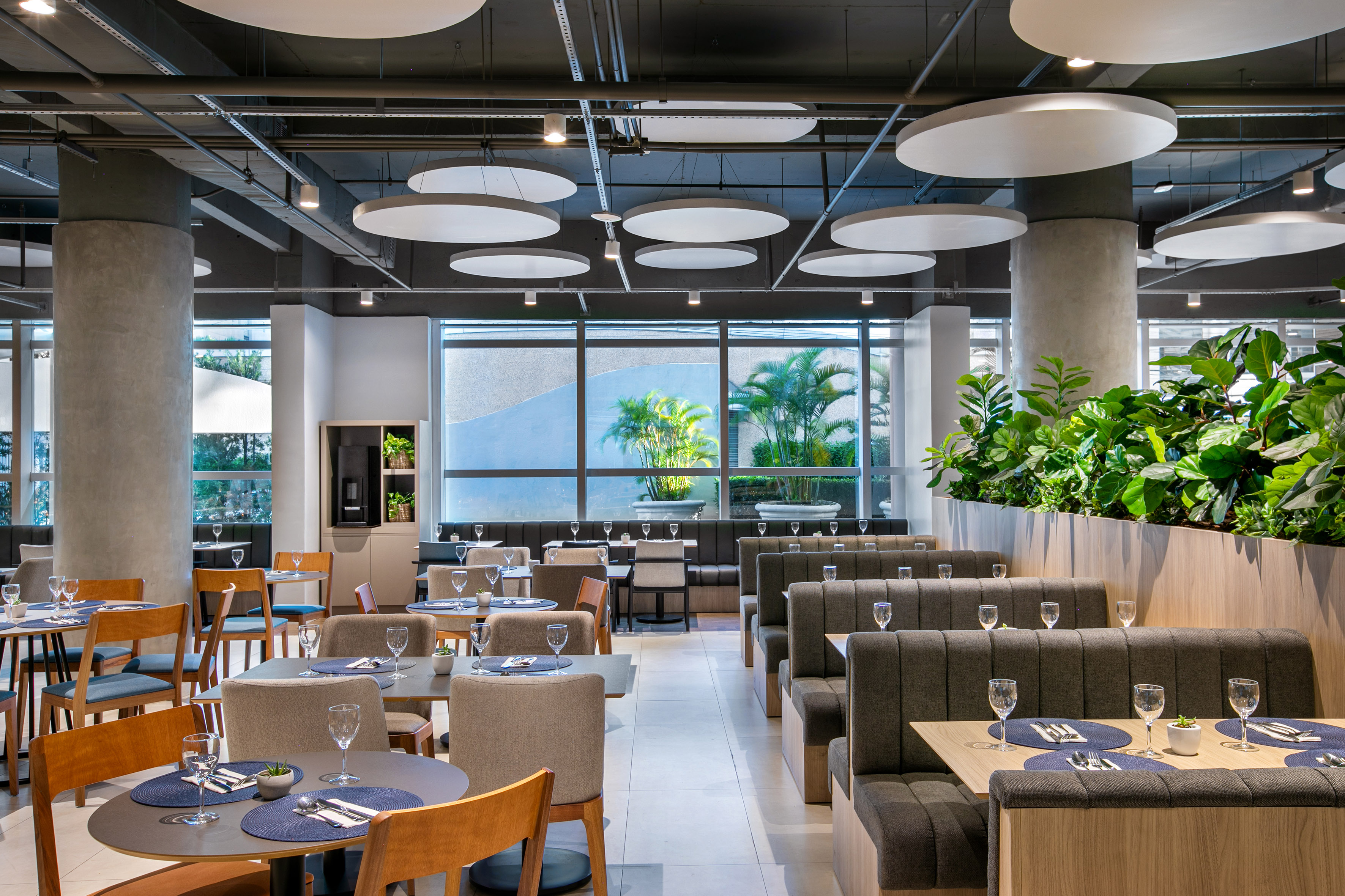 Modern restaurant with booth and table seating, large windows, and plants.