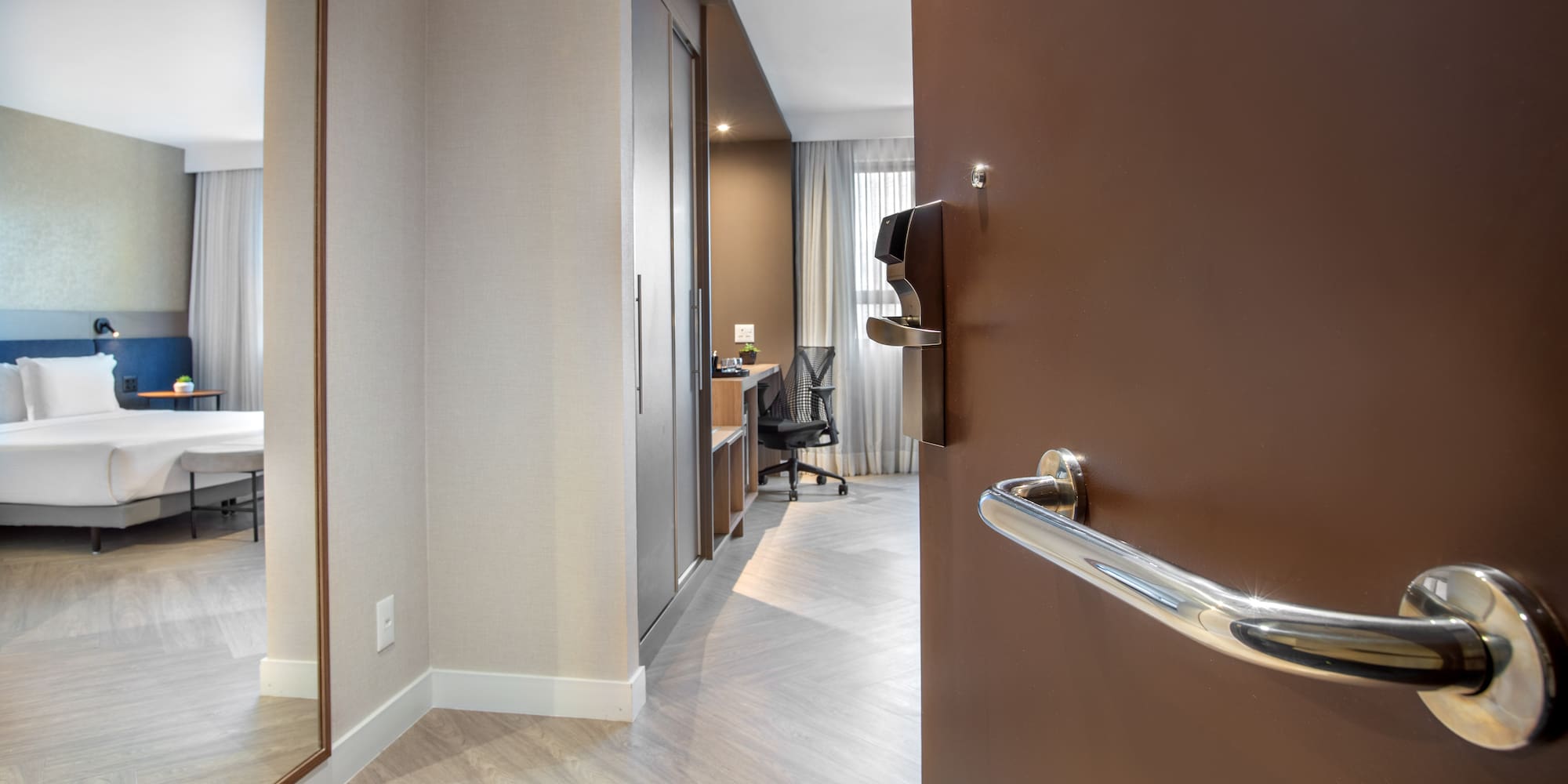 Entry view of modern hotel room with bed, desk, and full-length mirror.