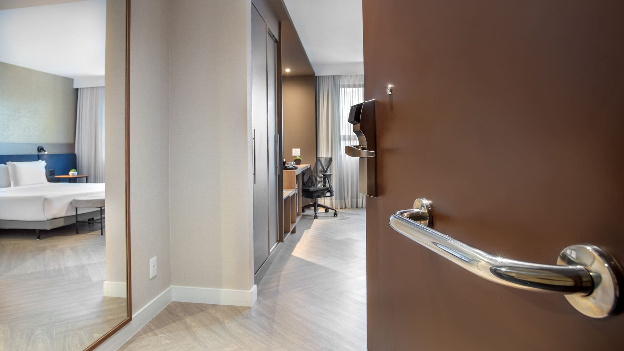 Entry view of modern hotel room with bed, desk, and full-length mirror.