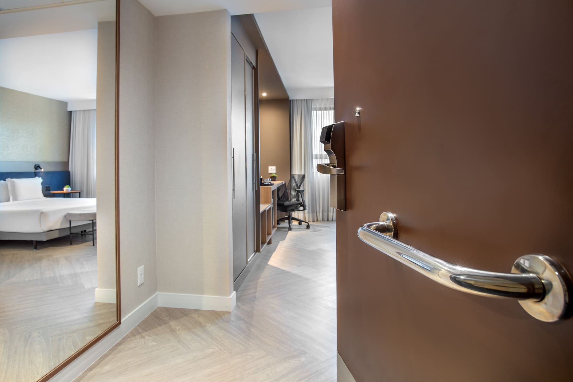 Entry view of modern hotel room with bed, desk, and full-length mirror.