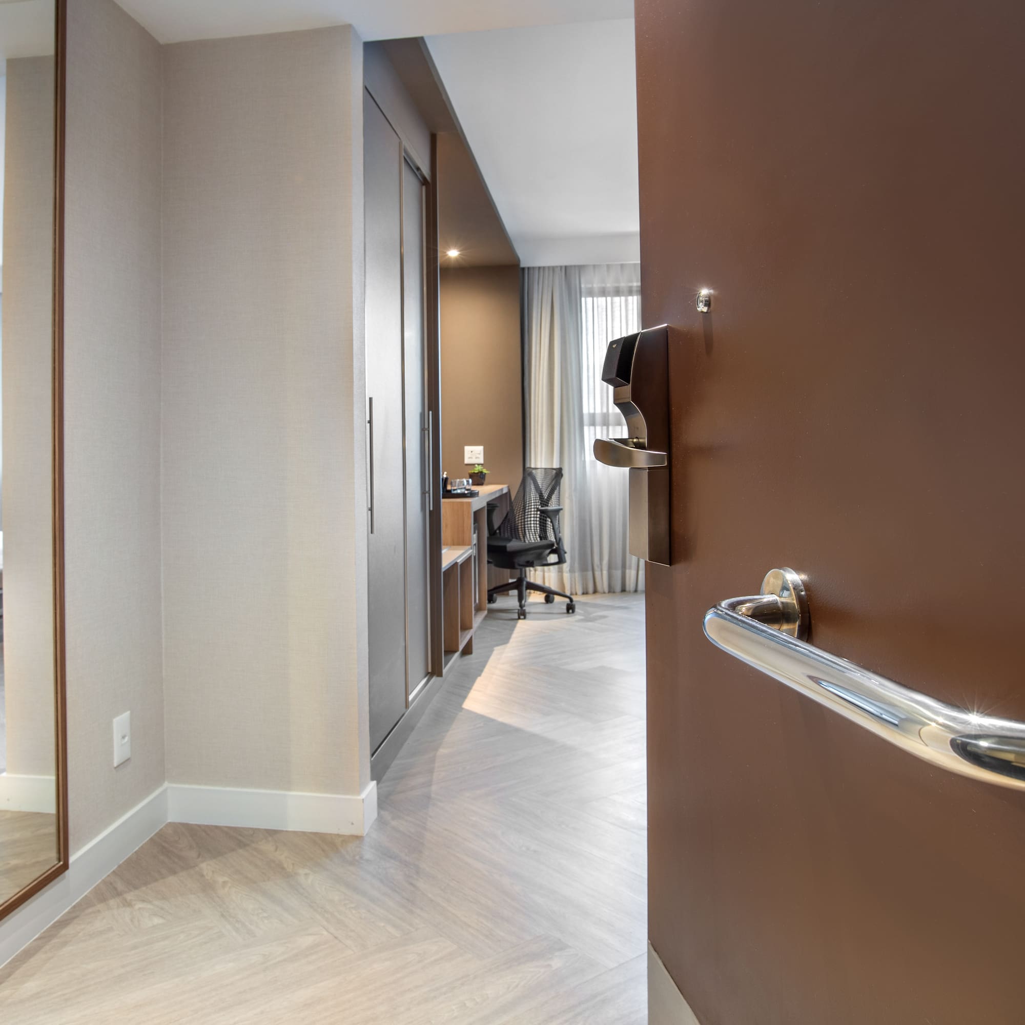 Entry view of modern hotel room with bed, desk, and full-length mirror.
