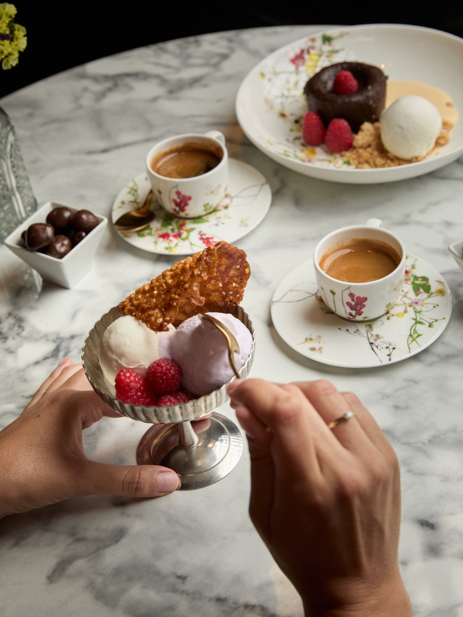 Dessert table: hands eating ice cream, chocolate lava cake, espresso coffee.