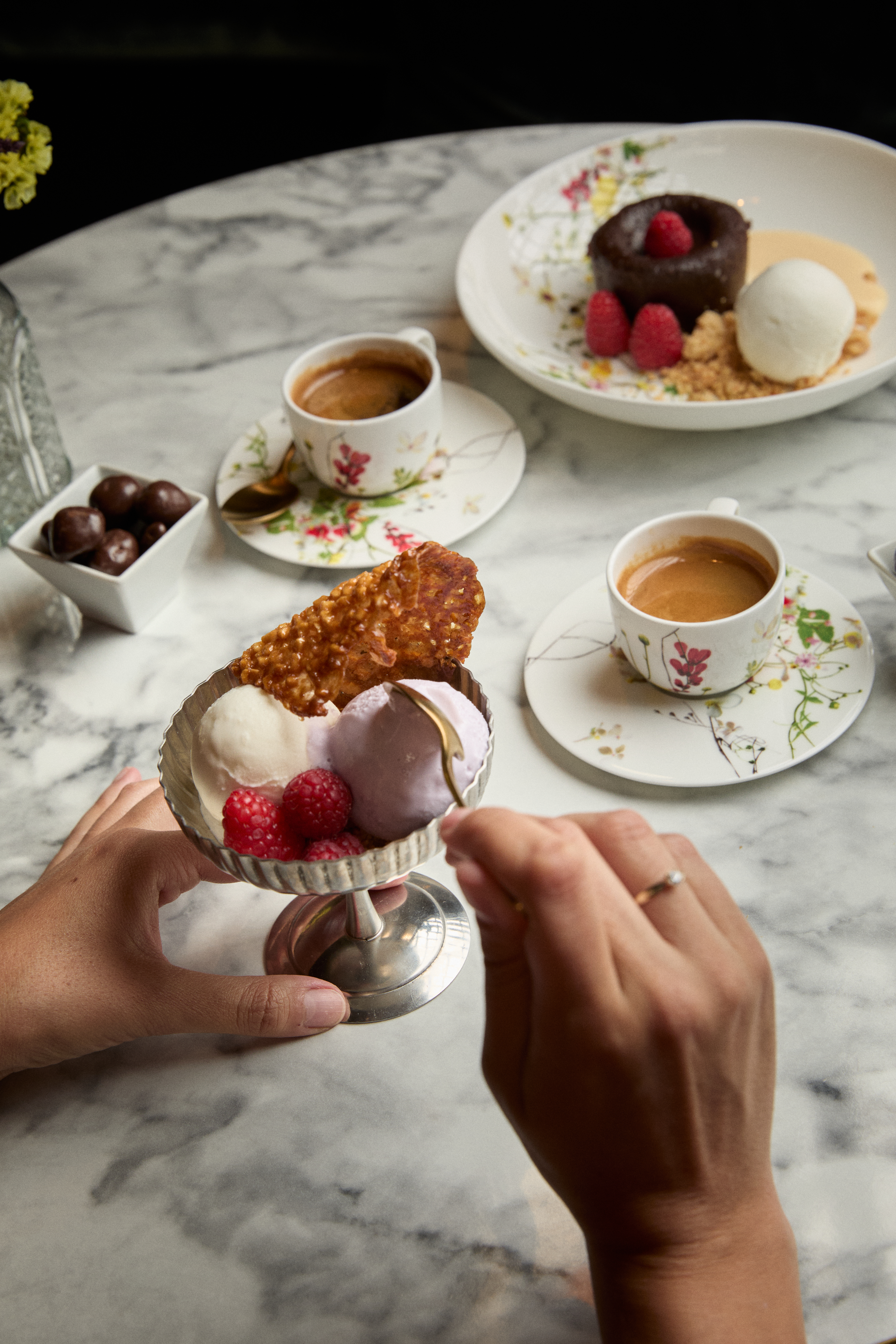Dessert table: hands eating ice cream, chocolate lava cake, espresso coffee.