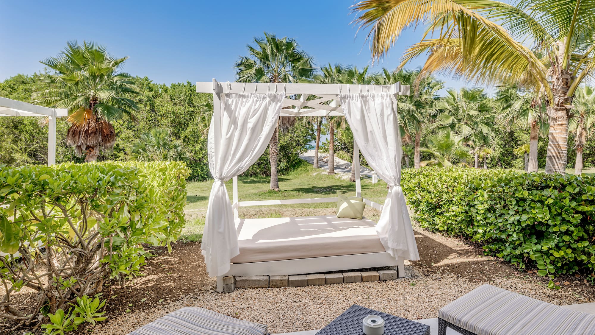 a bed with white curtains and a table in a garden