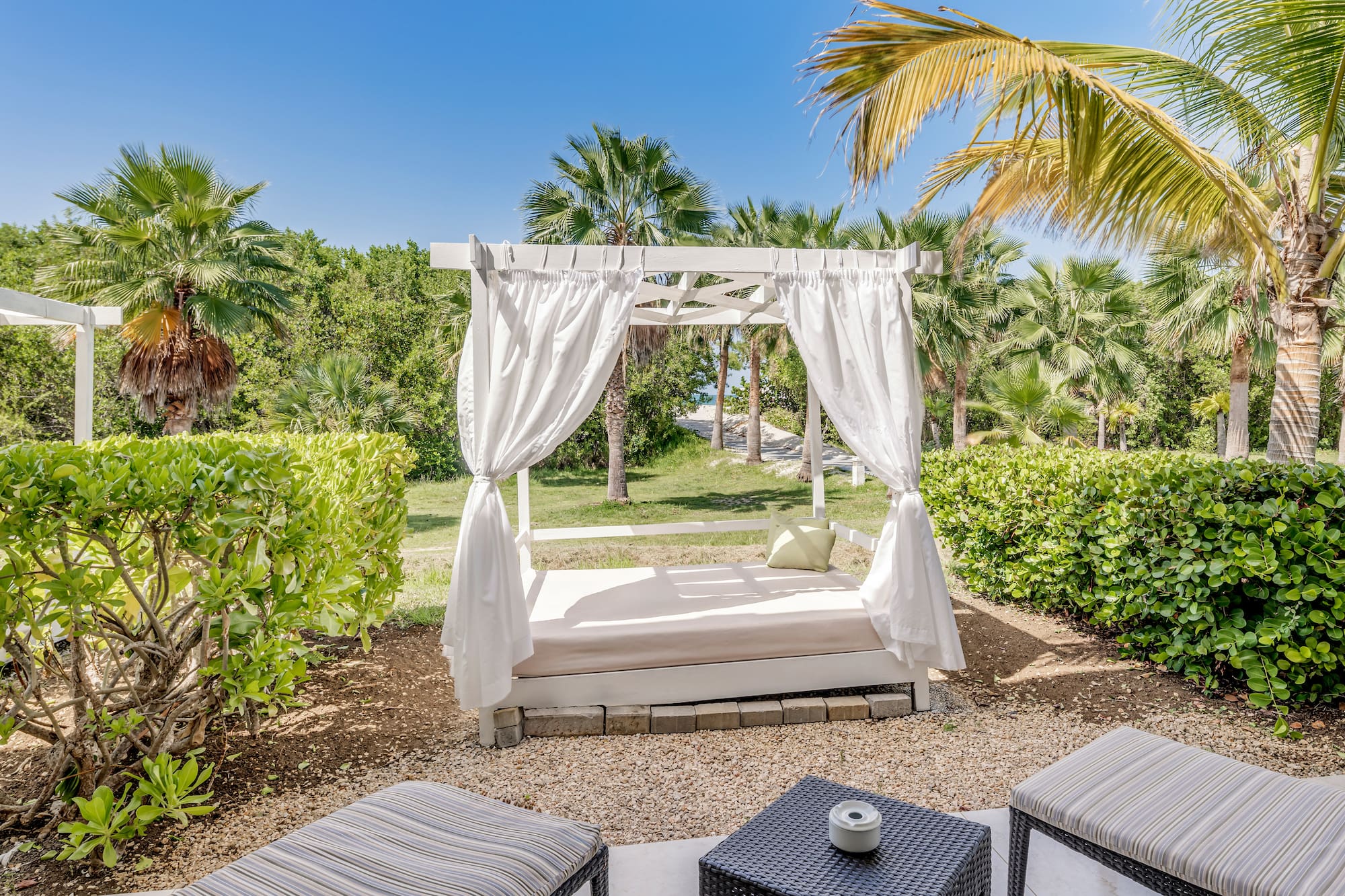 a bed with white curtains and a table in a garden