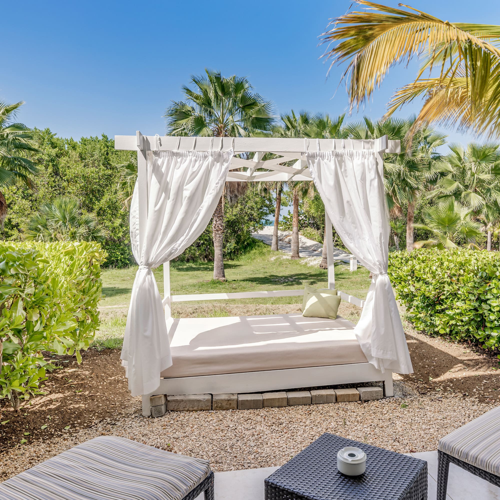 a bed with white curtains and a table in a garden