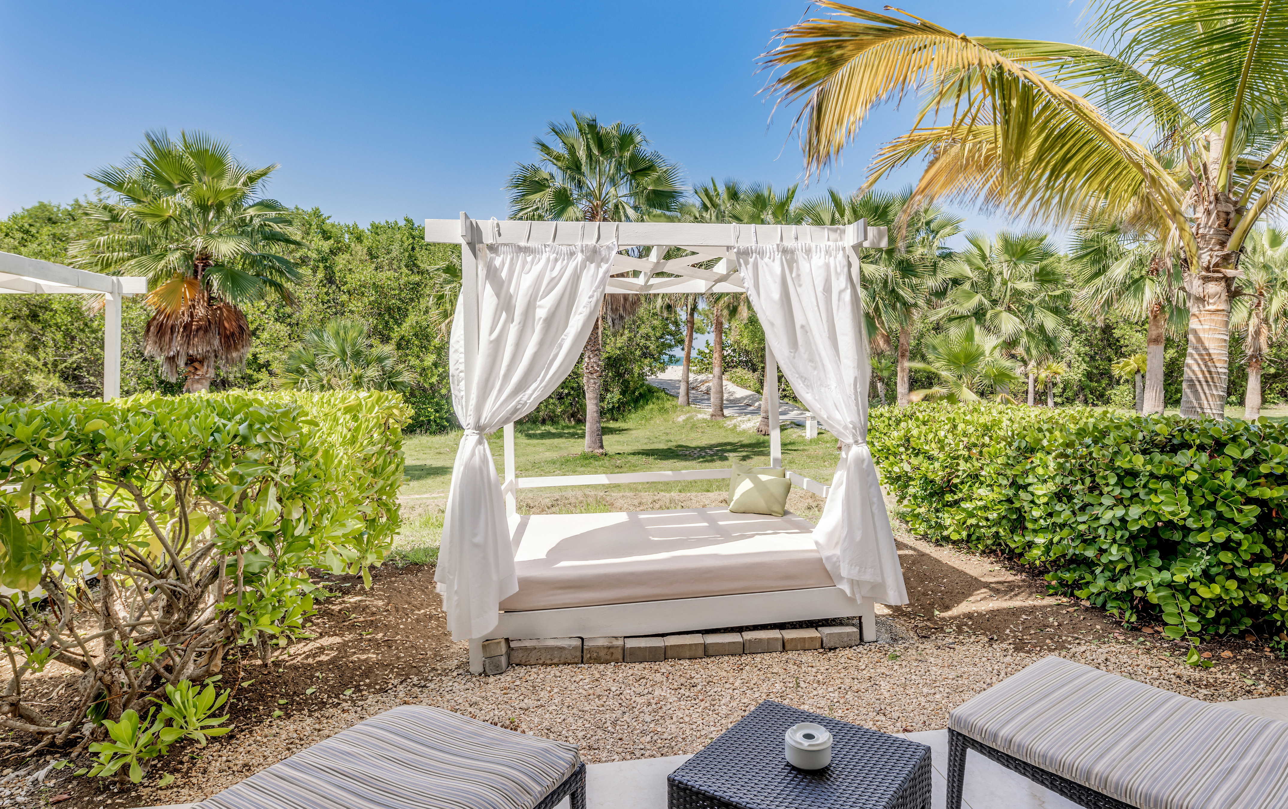 a bed with white curtains and a table in a garden