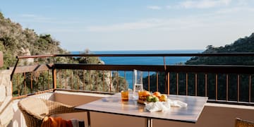 a table with fruit on it and a chair on a balcony overlooking the ocean