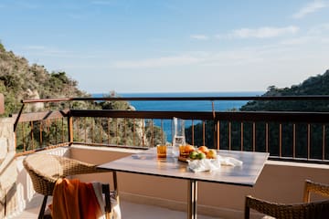 a table with fruit on it and a chair on a balcony overlooking the ocean