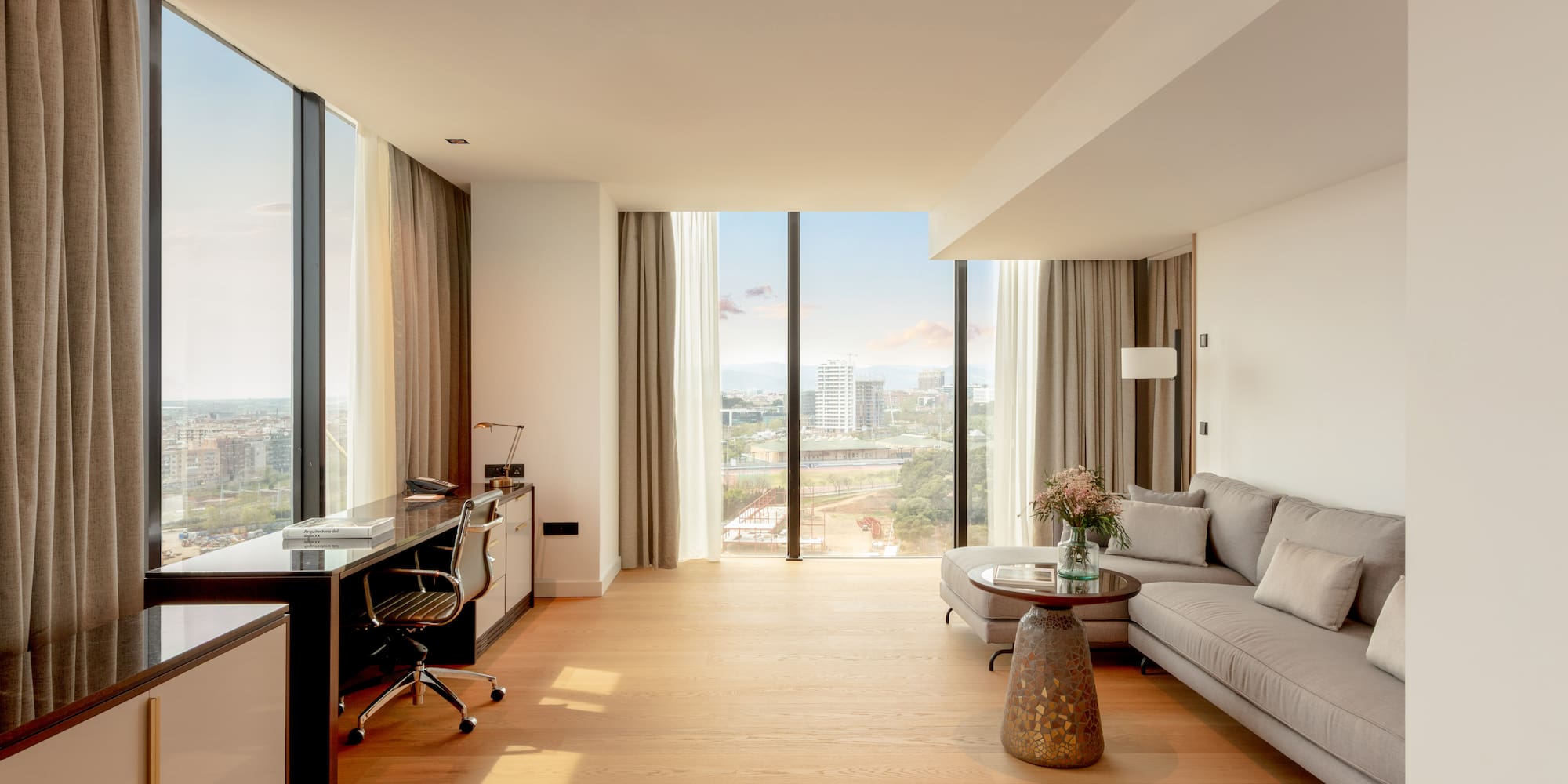 Bright modern suite with panoramic city views, living area, and workspace.
