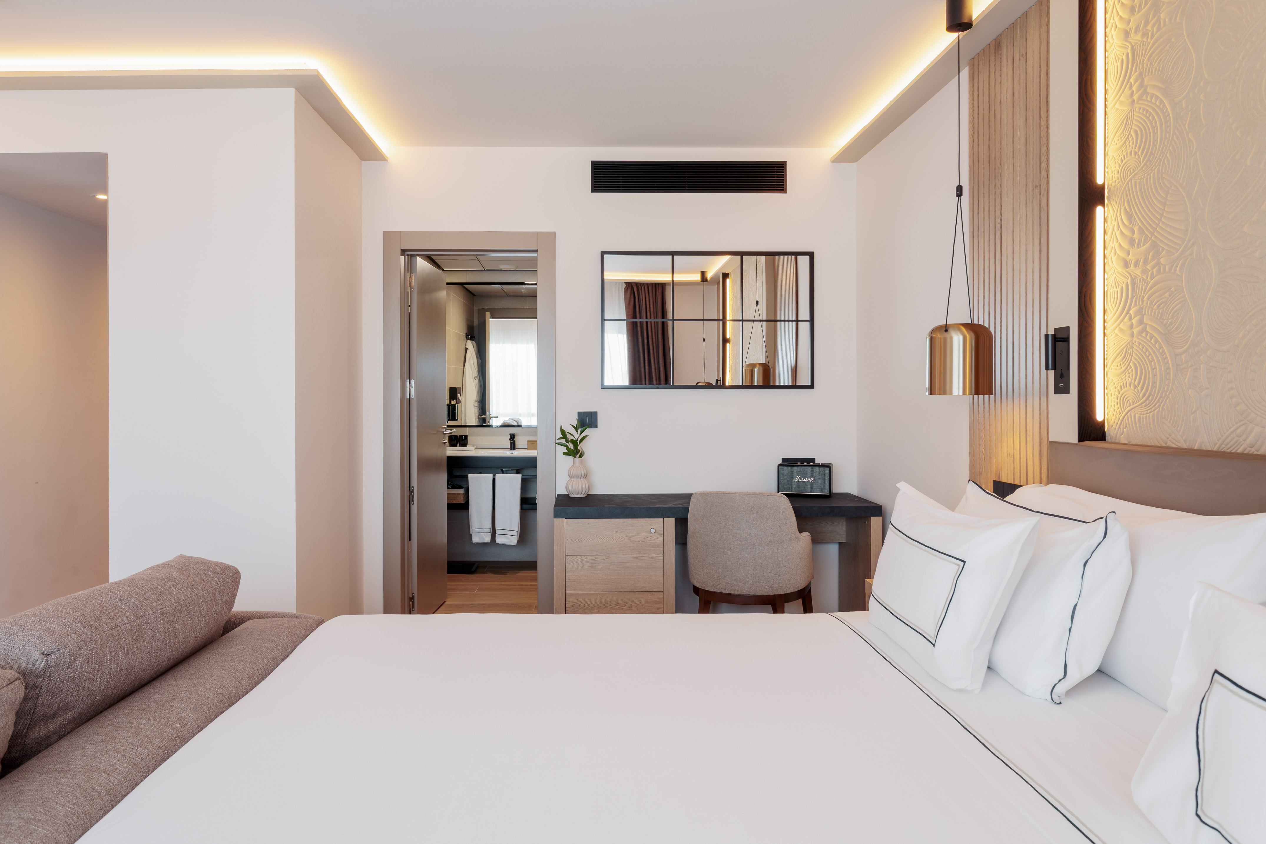 Modern luxury hotel bedroom with king bed, desk, and open ensuite bathroom.