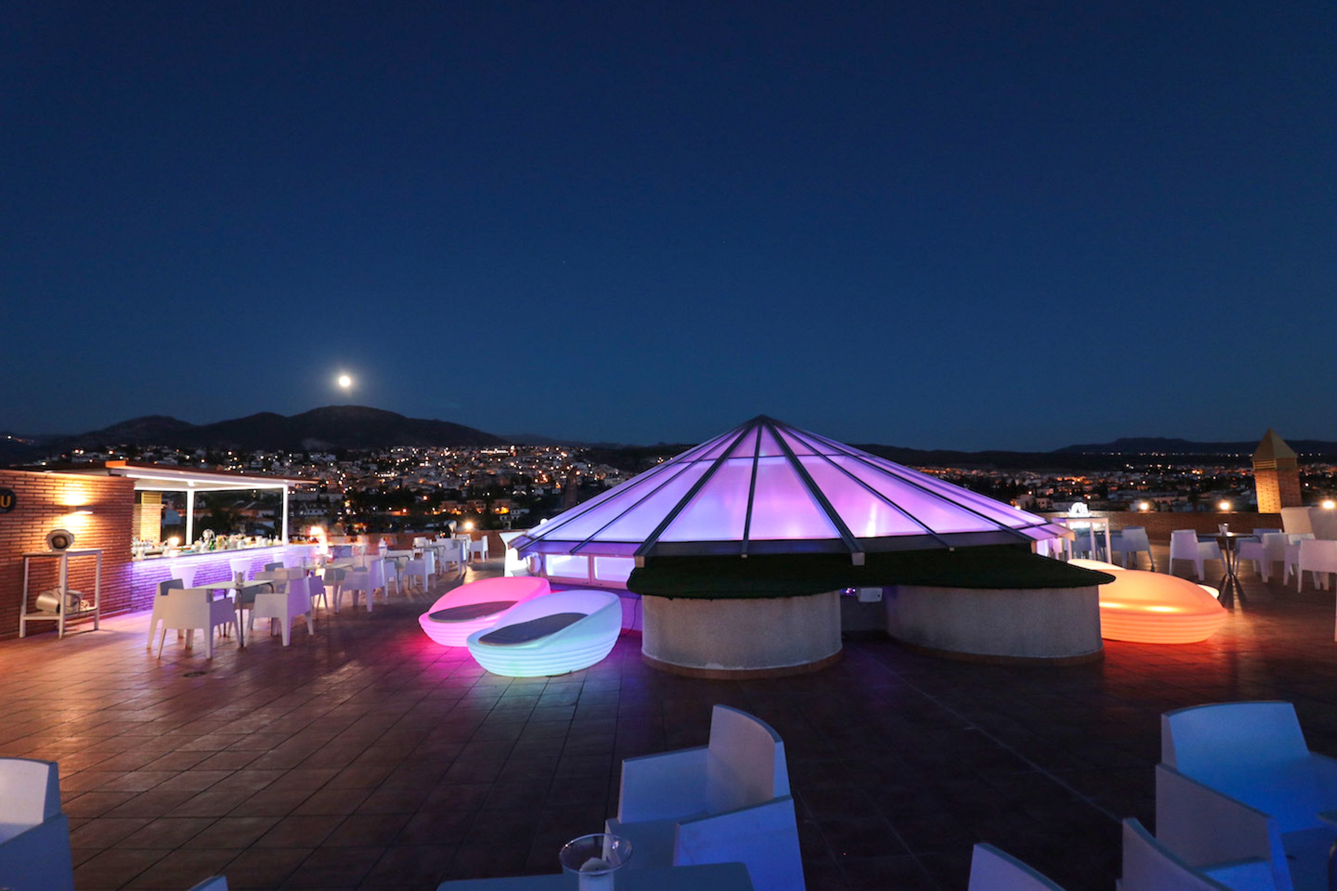 Chic rooftop bar lounge at night, glowing purple pyramid, city lights, moon.