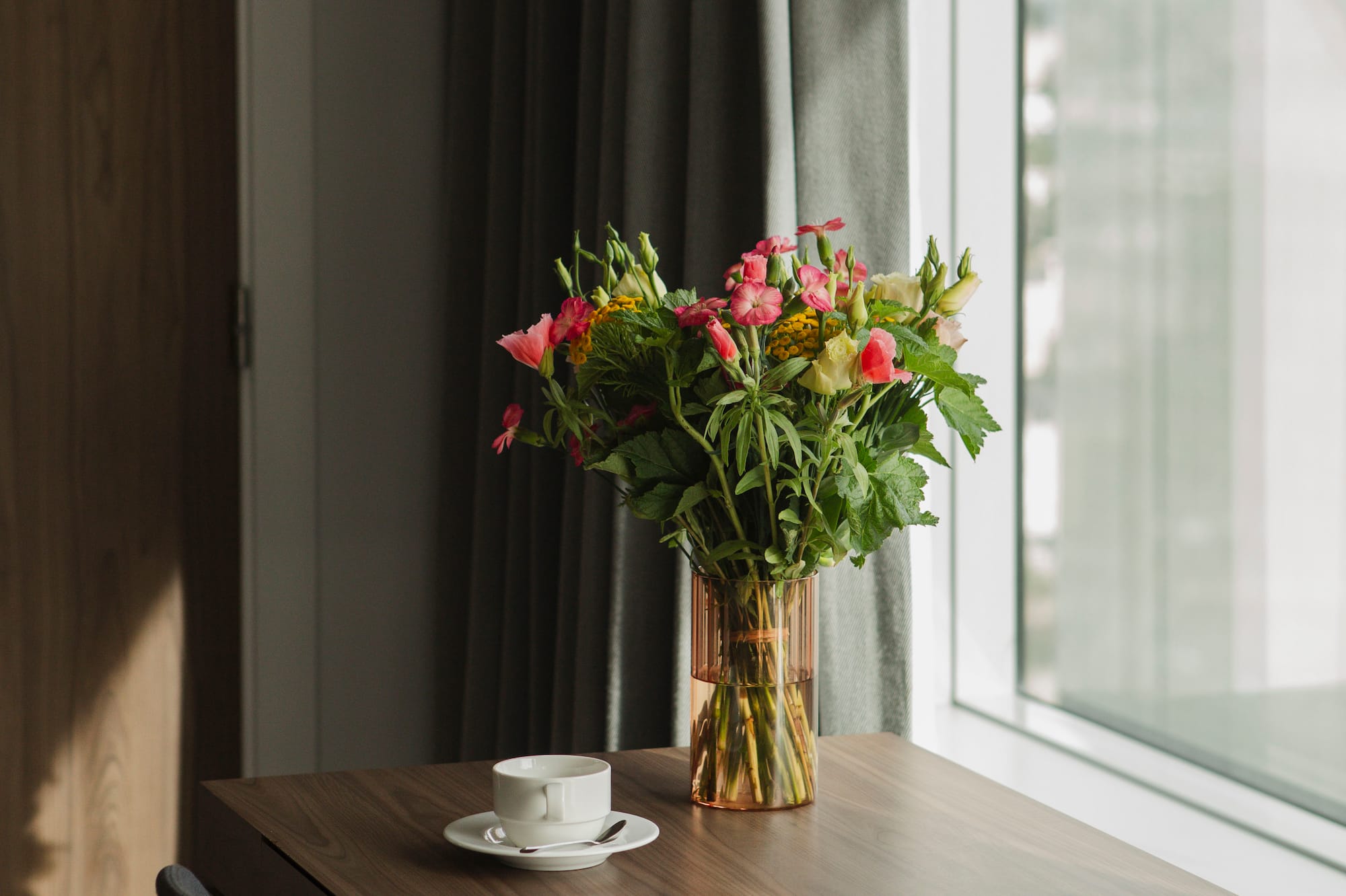 Colorful flower bouquet and coffee cup on wooden table near window with natural light.