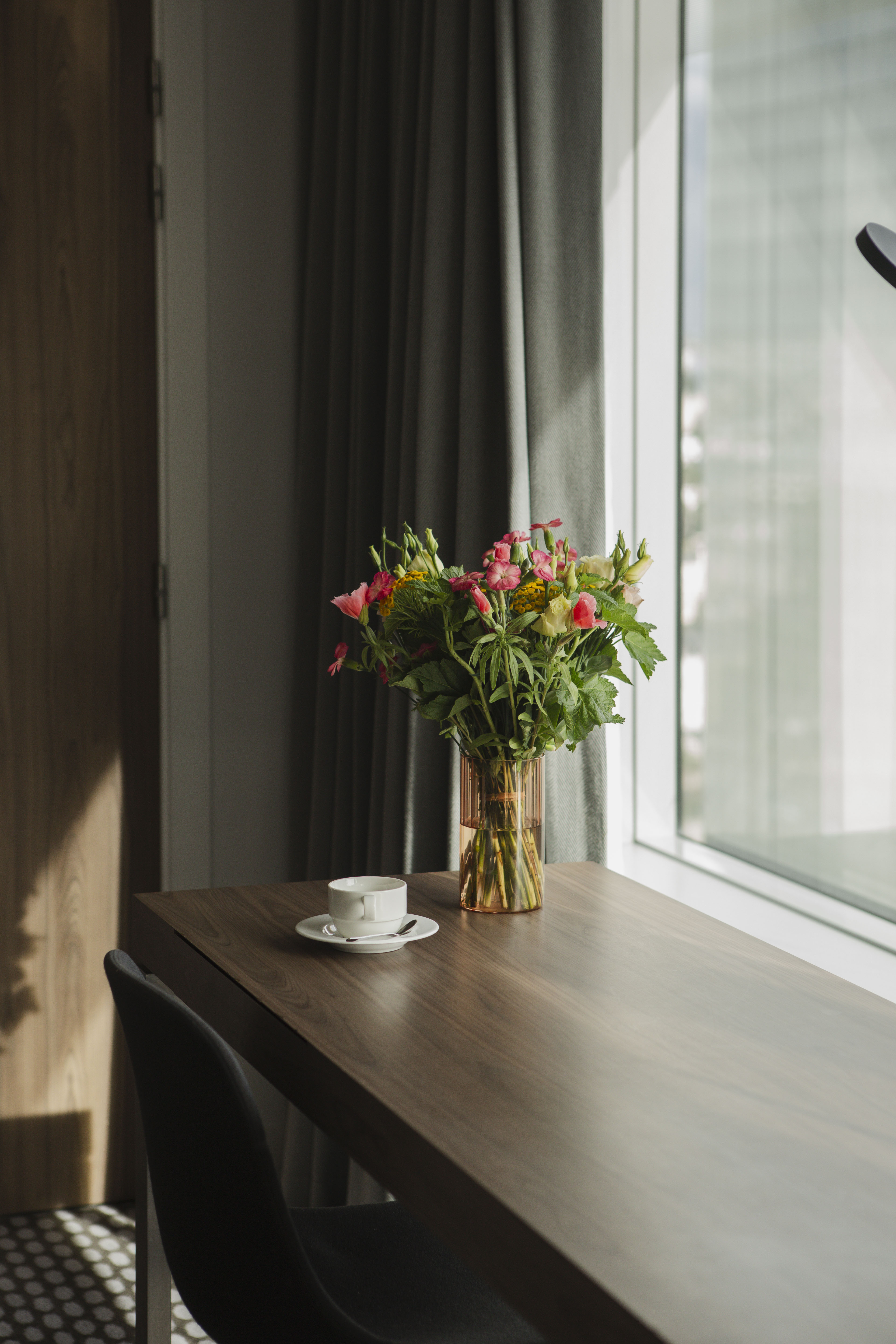 Colorful flower bouquet and coffee cup on wooden table near window with natural light.