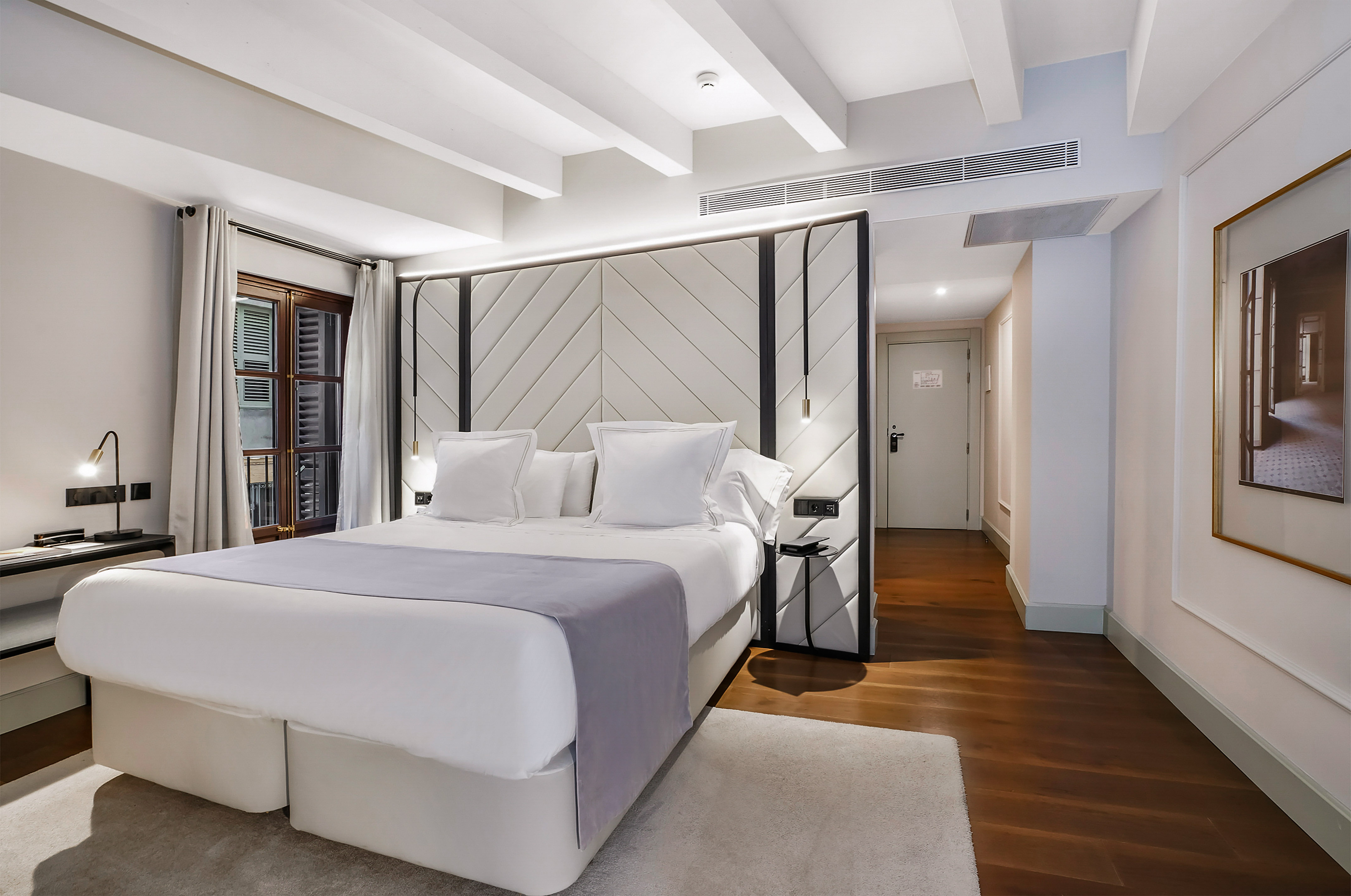 Elegant hotel bedroom featuring a large bed, geometric headboard, and wood floor.
