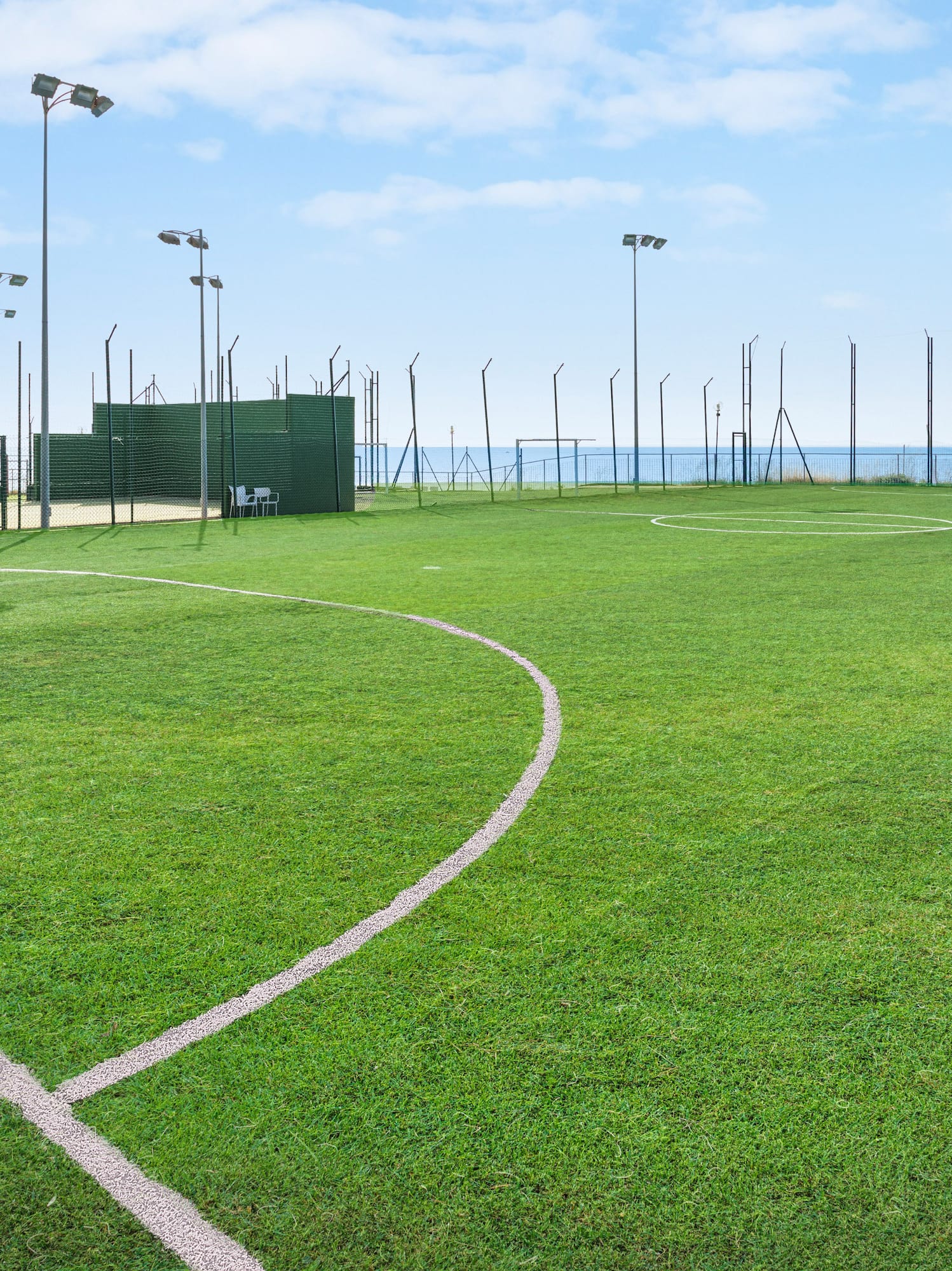 Artificial turf soccer field with white lines, goal, floodlights, and sea view.