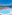 Resort swimming pool, blue sea, mountains, palm trees, lounge chairs.