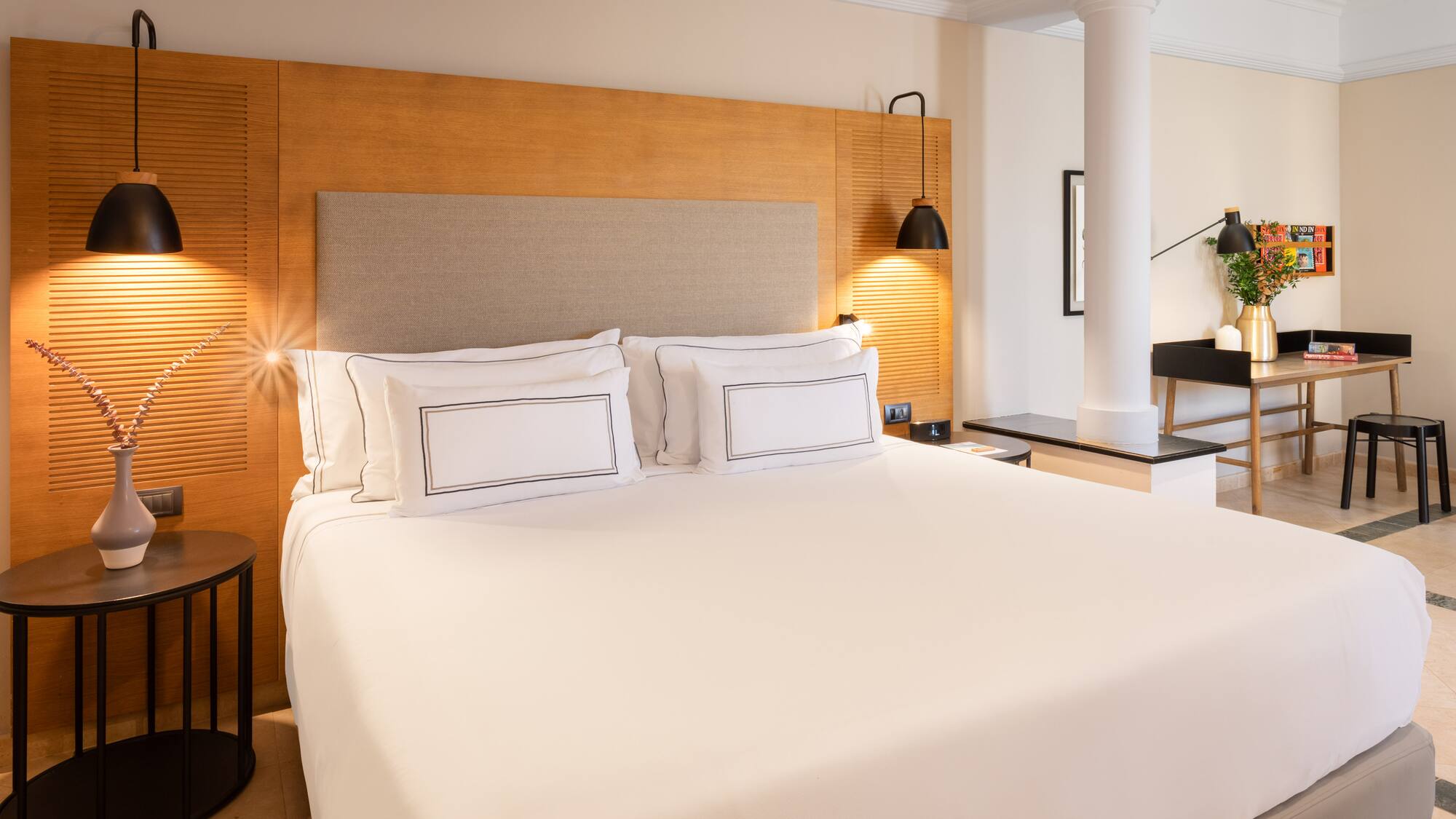 a bed with white sheets and a wood headboard in a room with columns