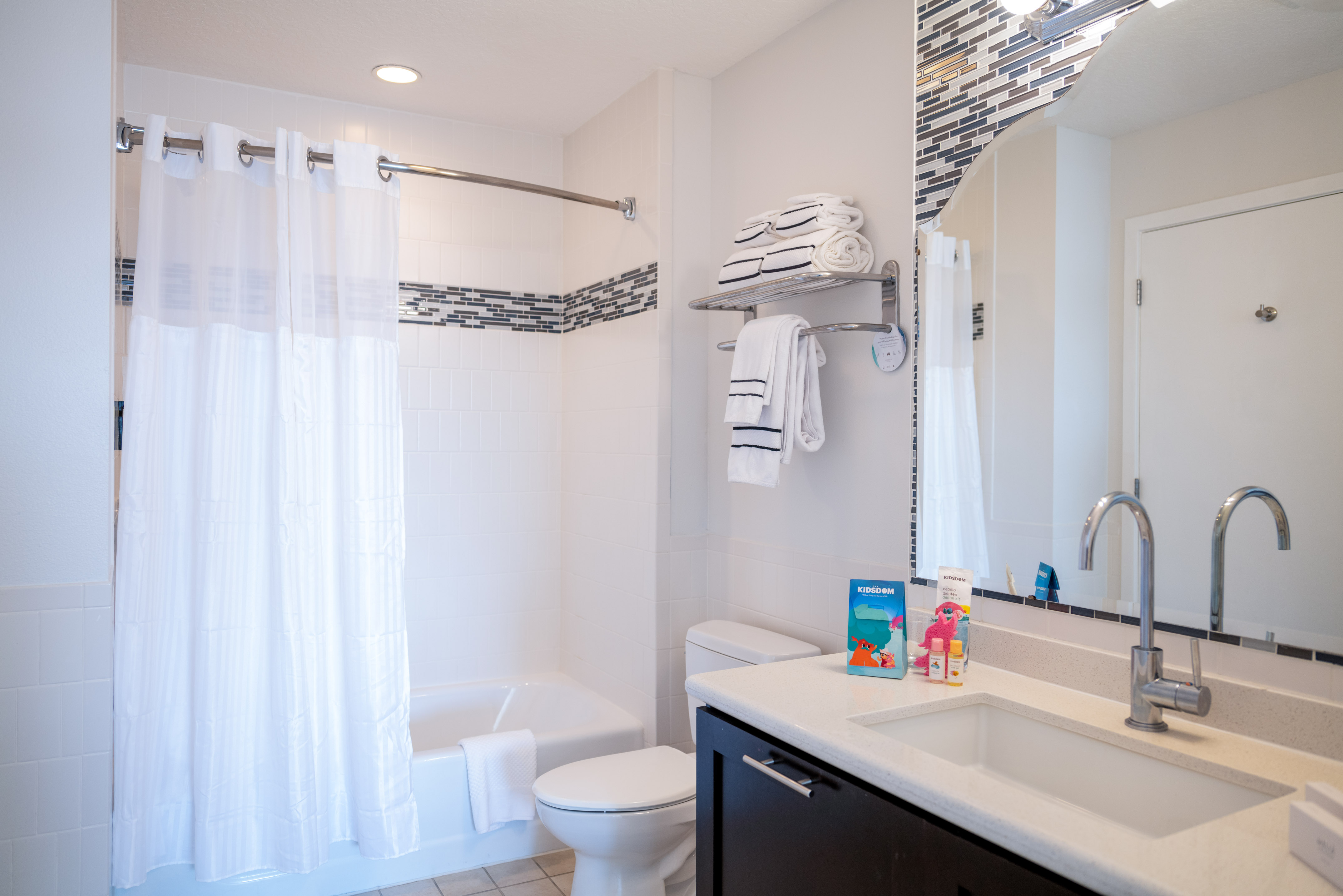 Modern white hotel bathroom featuring shower/tub, toilet, vanity, and fresh towels.