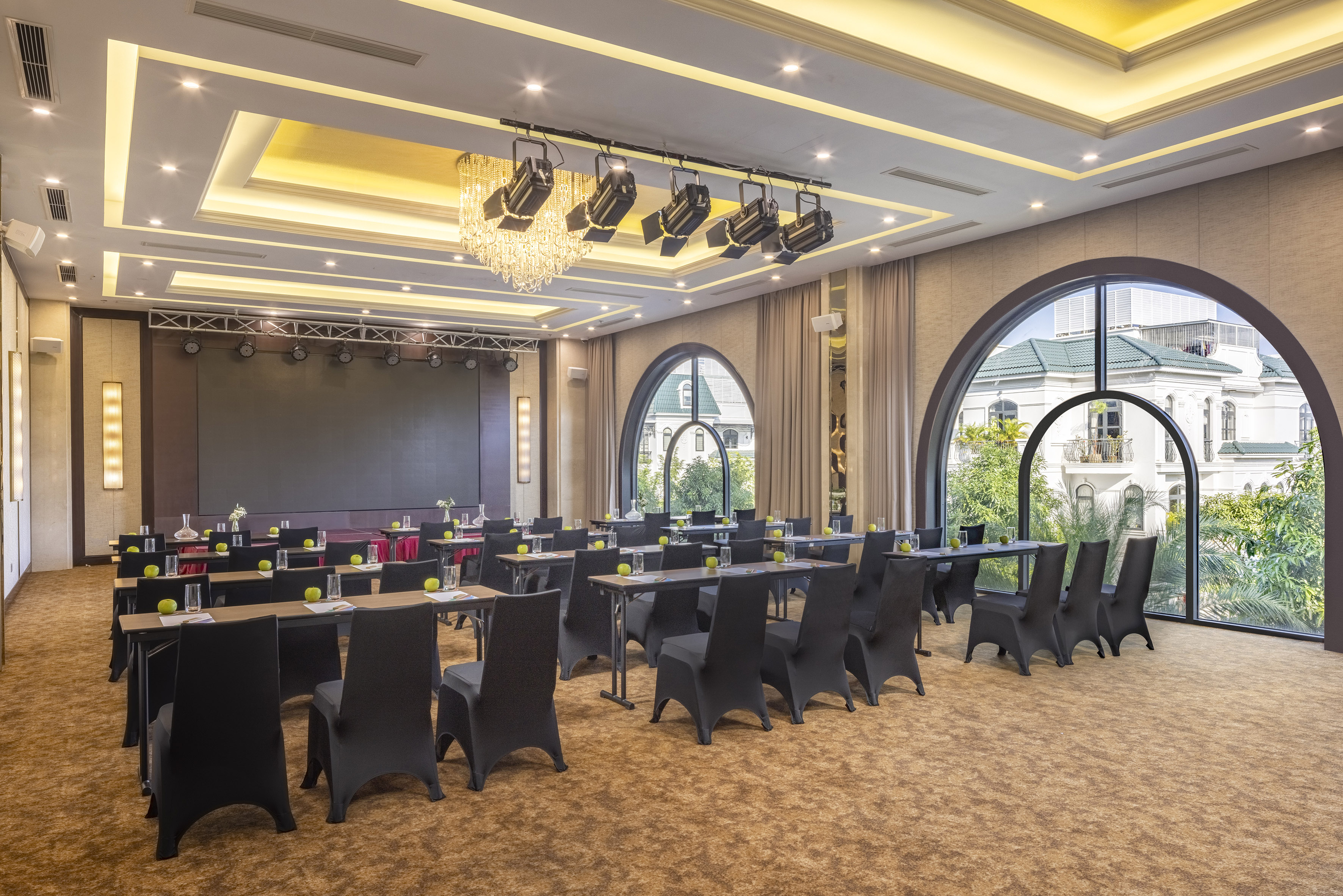 Elegant hotel conference room with classroom setup, large screen, arched windows.