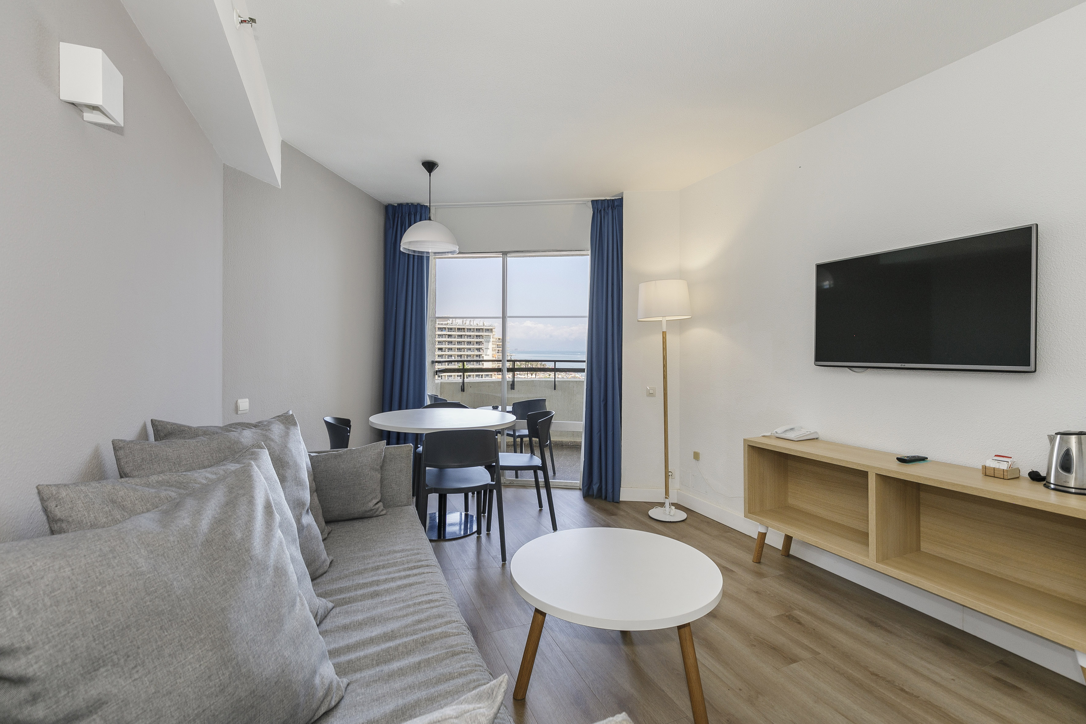 Modern apartment living room with sofa, dining area, balcony, and sea view.