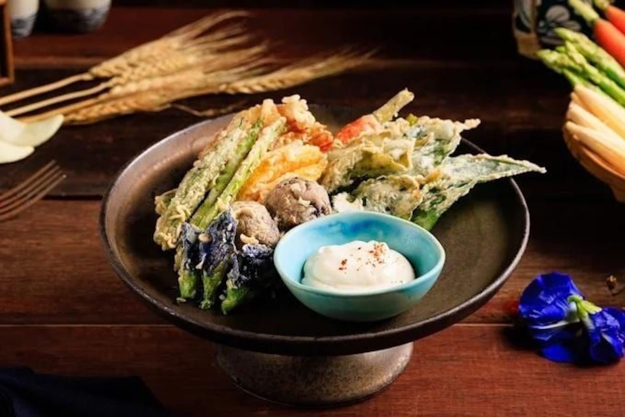 Mixed vegetable tempura with creamy dipping sauce on a dark serving stand.