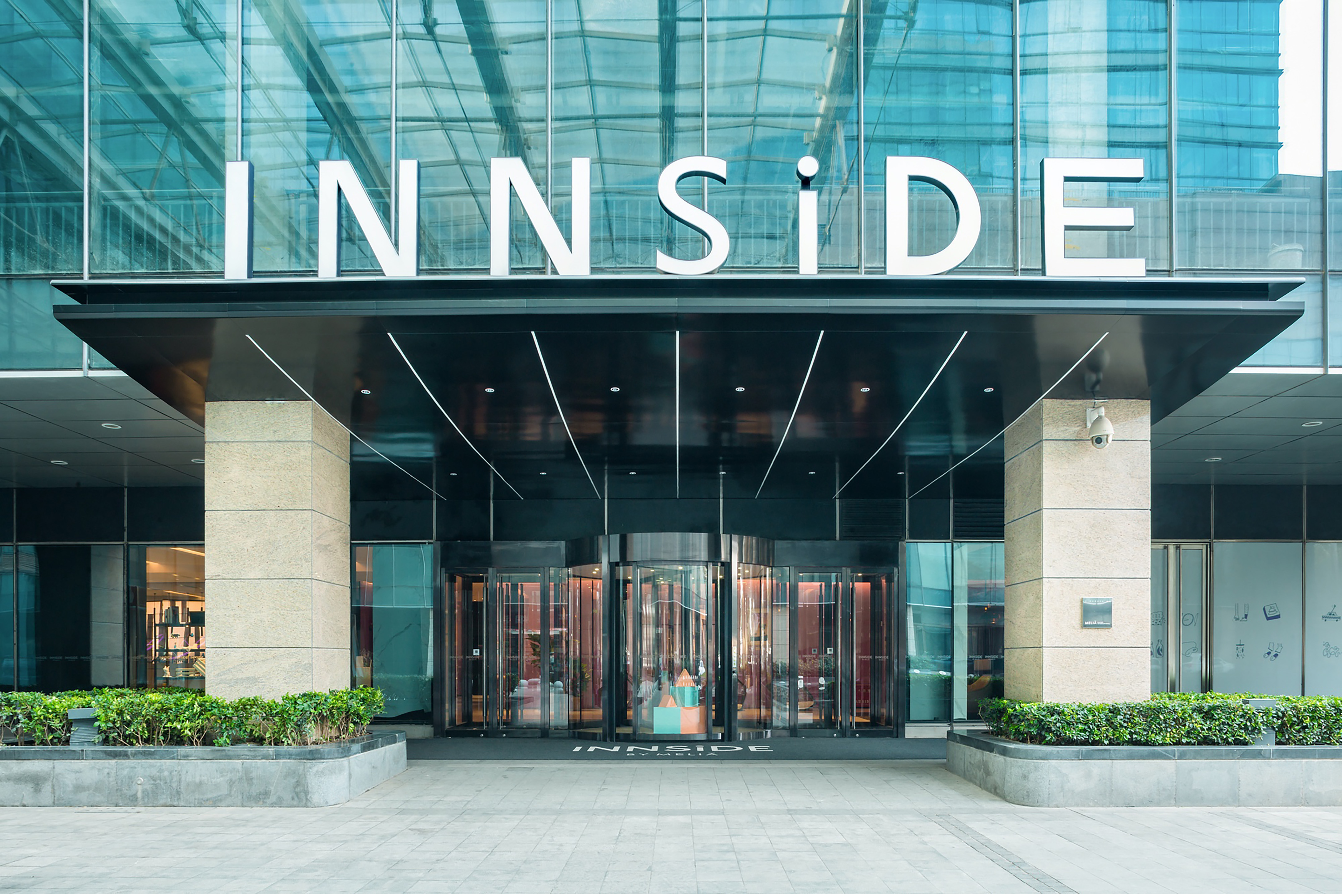 Modern INNSIDE hotel entrance, glass facade, white sign, and revolving doors.