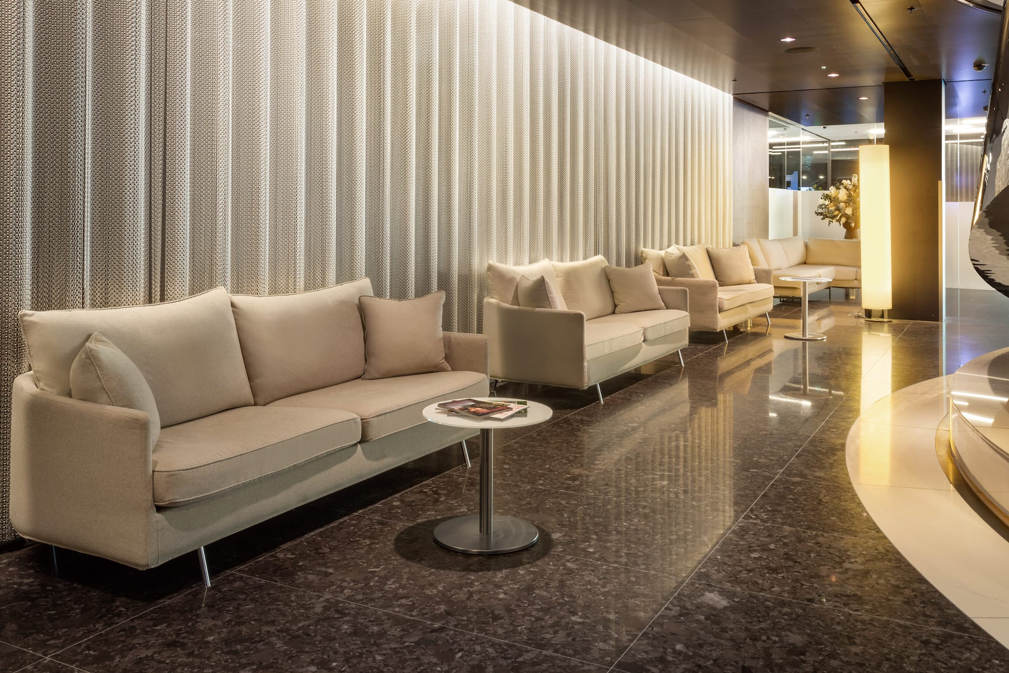Modern hotel lobby with beige sofas, dark polished floor, and textured wall panels.