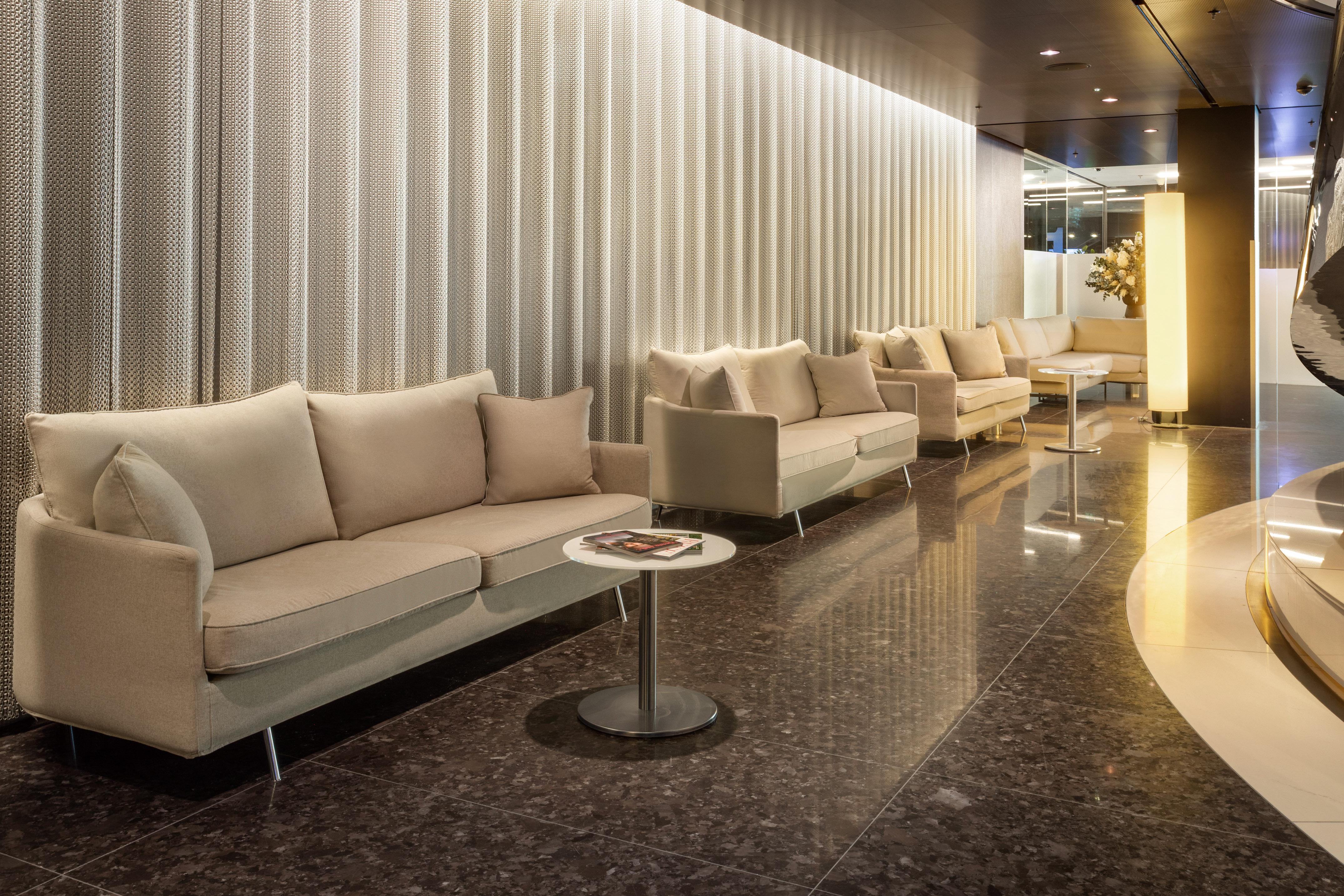 Modern hotel lobby with beige sofas, dark polished floor, and textured wall panels.