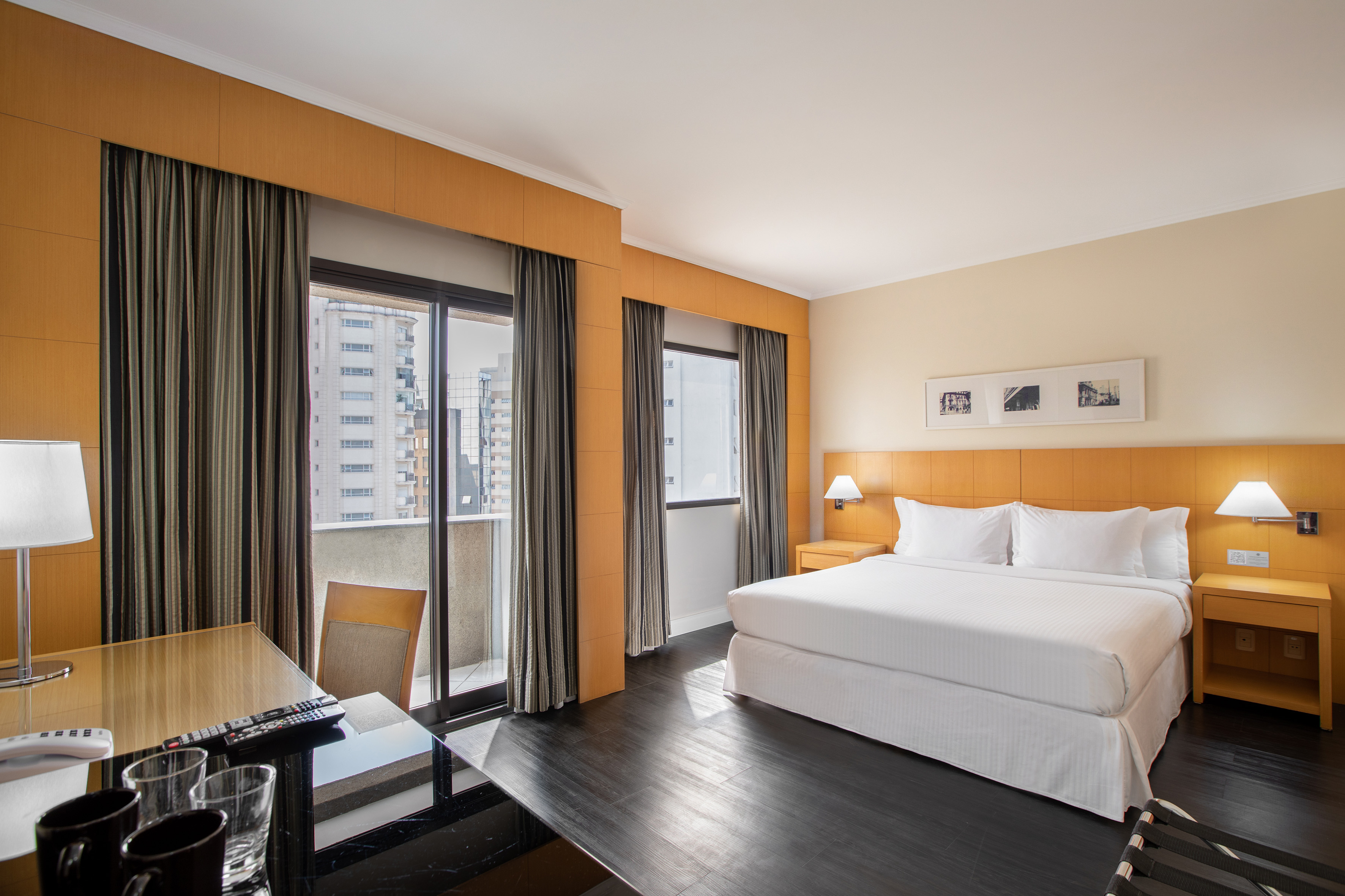Spacious hotel room featuring a king bed, desk, and balcony with city views.