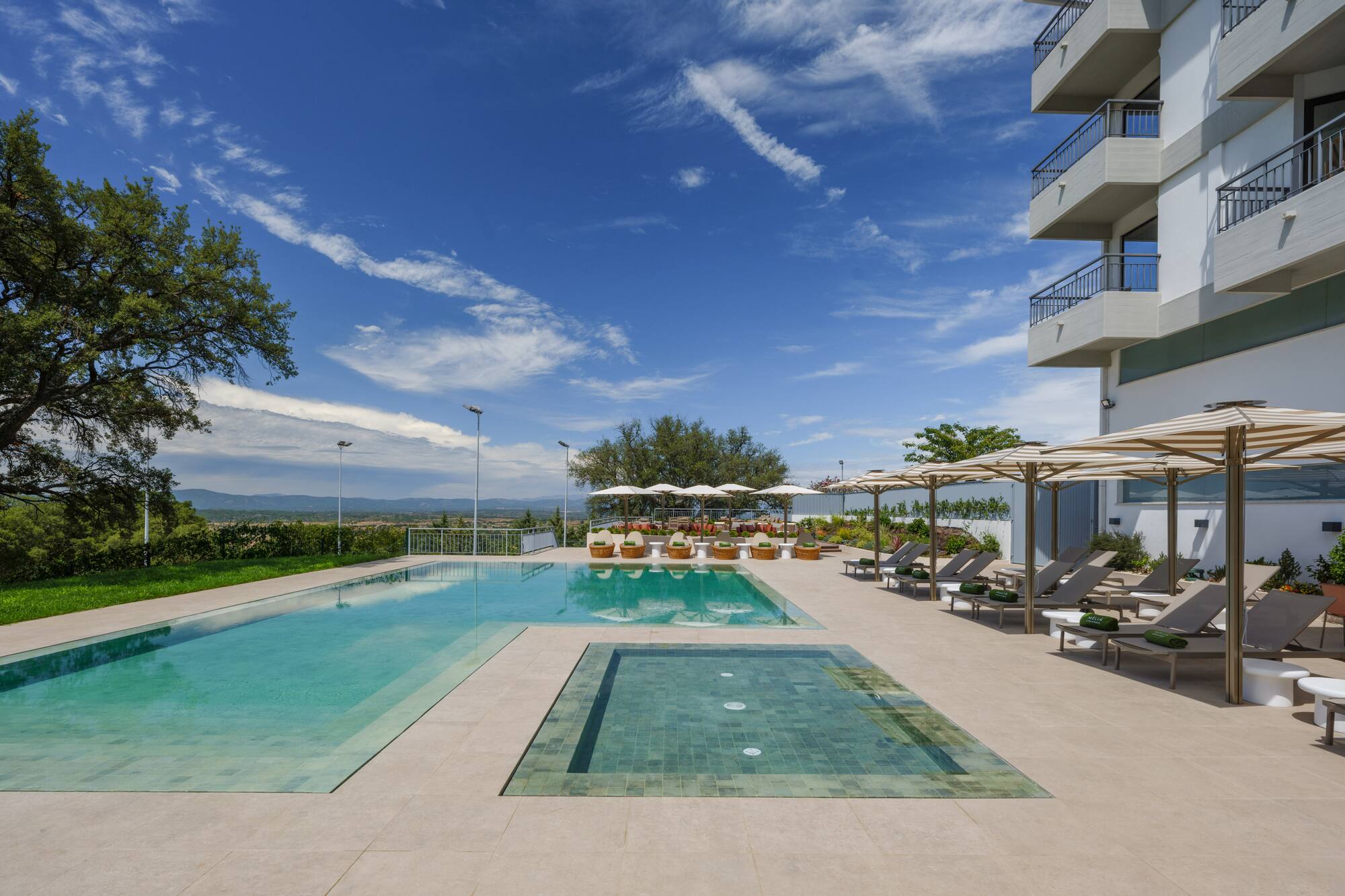Resort outdoor pool with lounge chairs, striped umbrellas, and modern hotel.