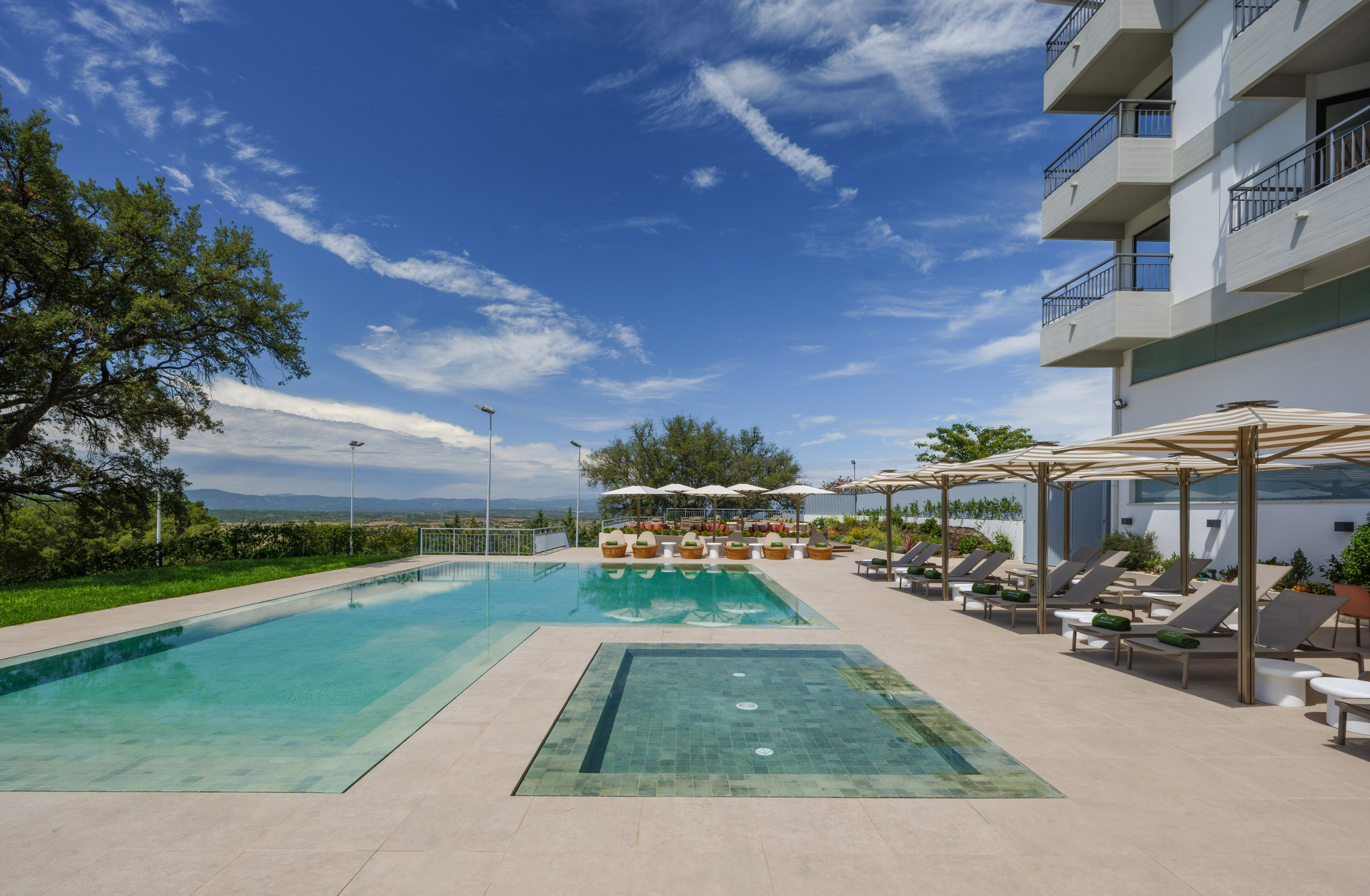 Resort outdoor pool with lounge chairs, striped umbrellas, and modern hotel.