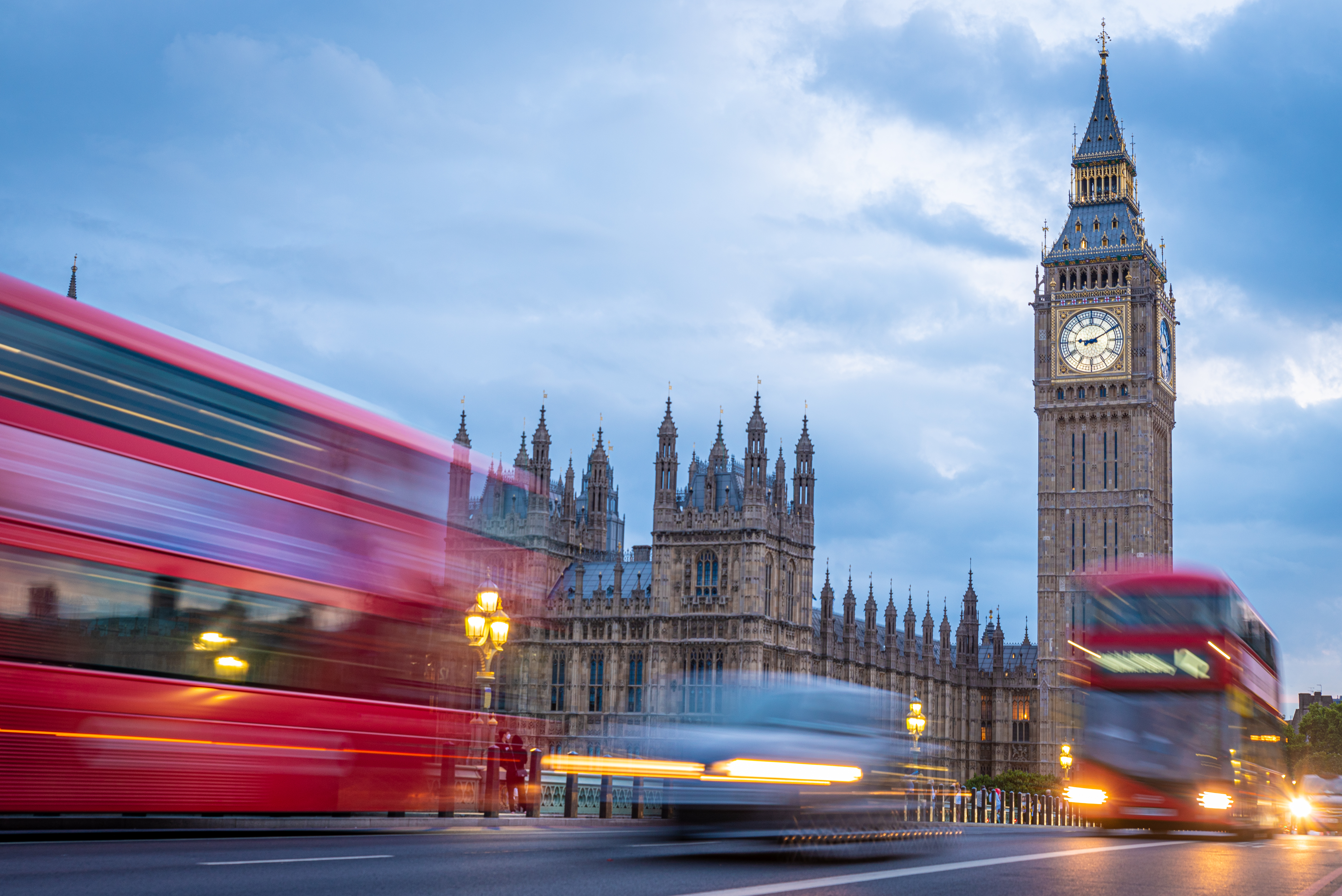 Big Ben y Parlamento de Londres al atardecer con autobuses rojos en movimiento.