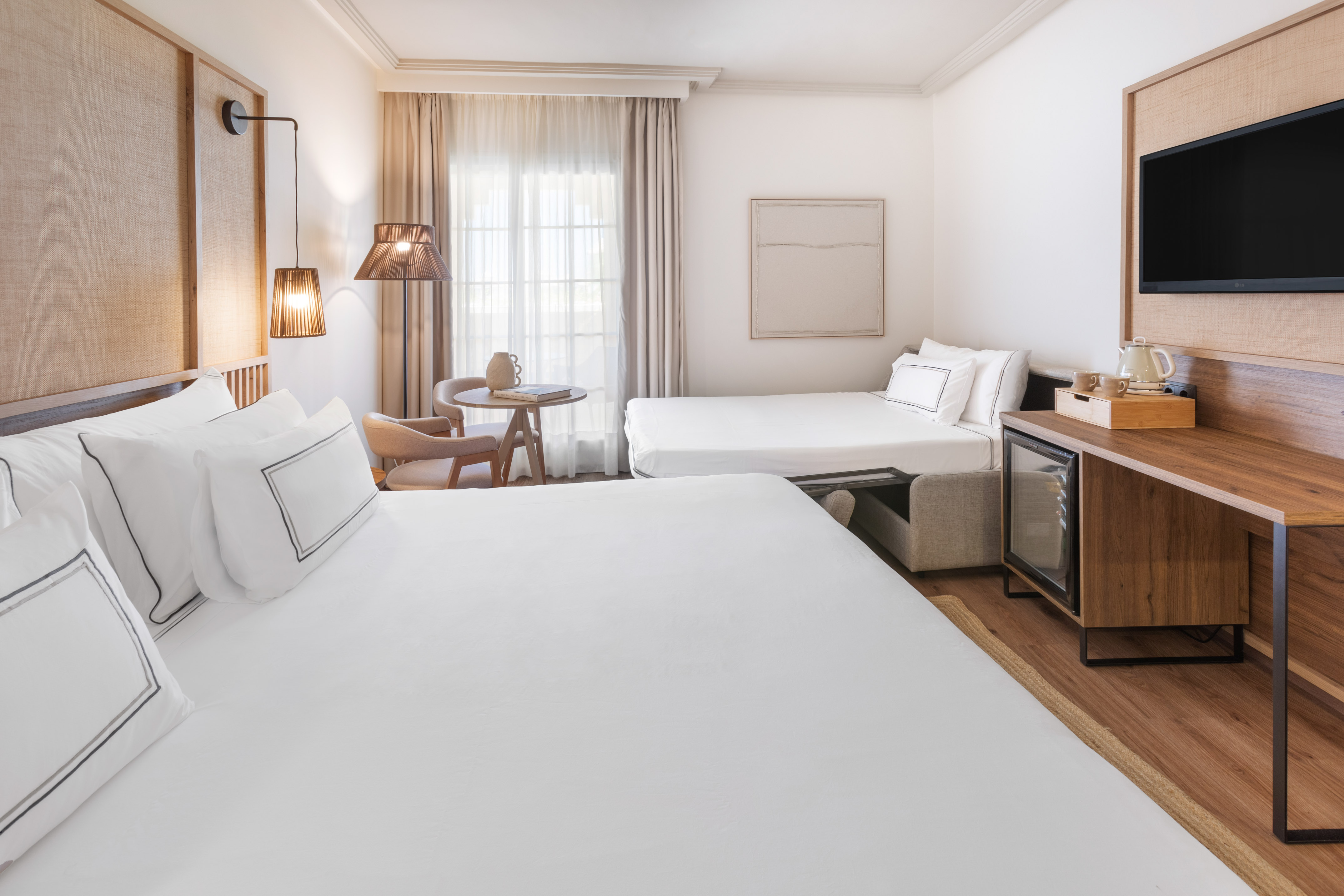 Modern hotel room with large bed, sofa bed, TV, desk, and bright, clean design.
