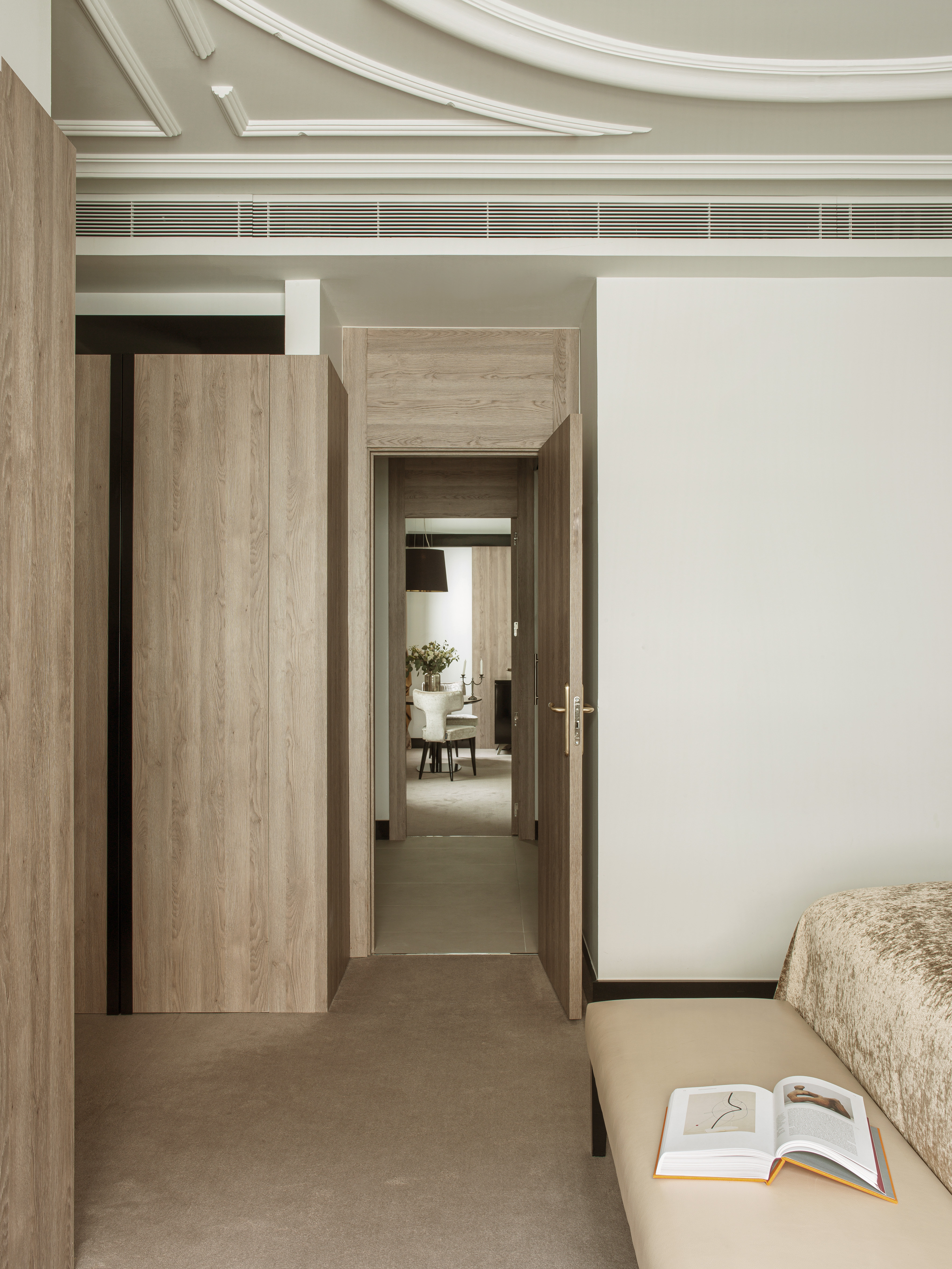Modern bedroom with wood paneling, open door to dining area, book on bench.