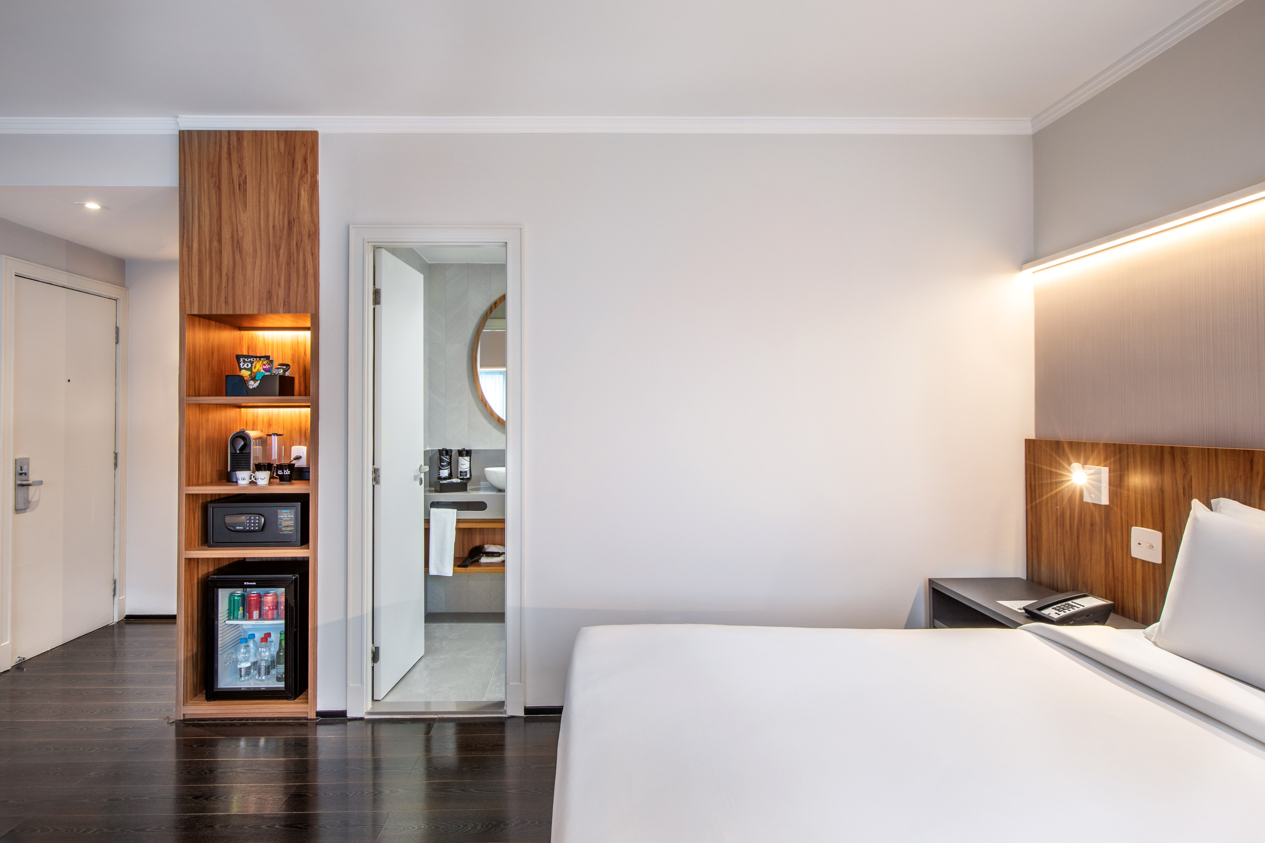 Modern hotel room with bed, built-in minibar, coffee machine, and bathroom entrance.